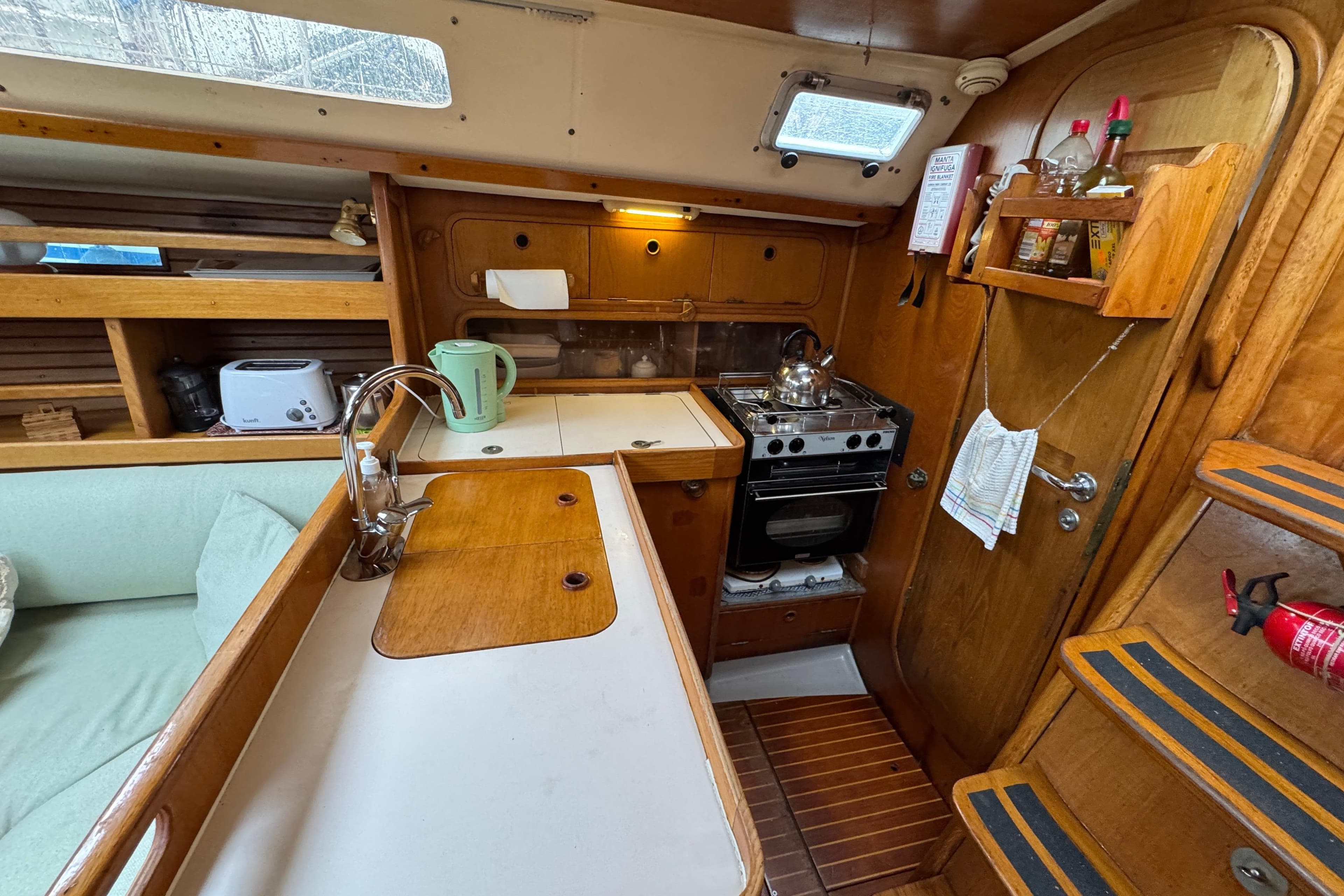Interior of 1988 Beneteau Oceanis 390 sailboat kitchen with wooden cabinetry and appliances.