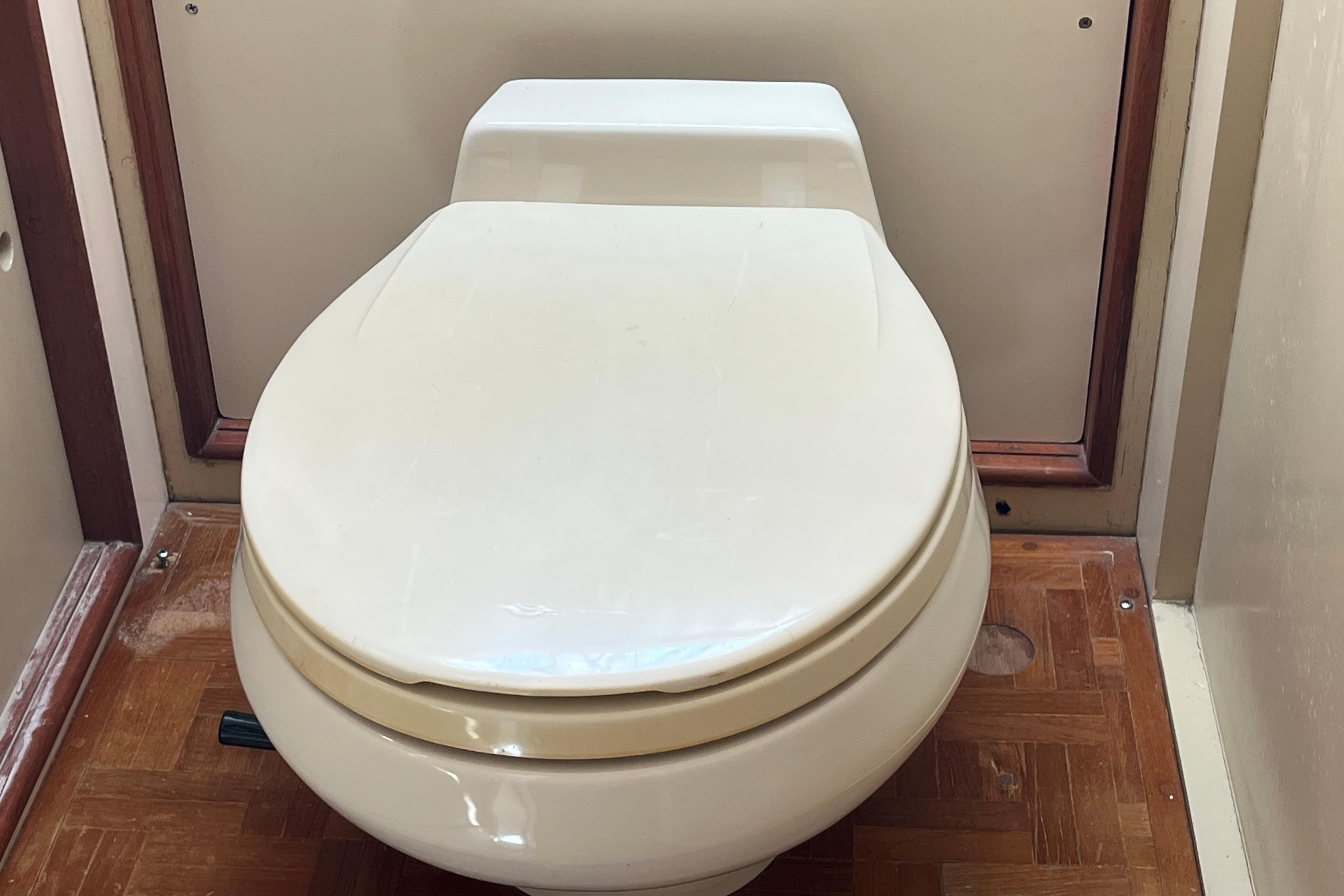 Toilet in 1979 Grand Banks 36 Classic boat interior, featuring wooden flooring.