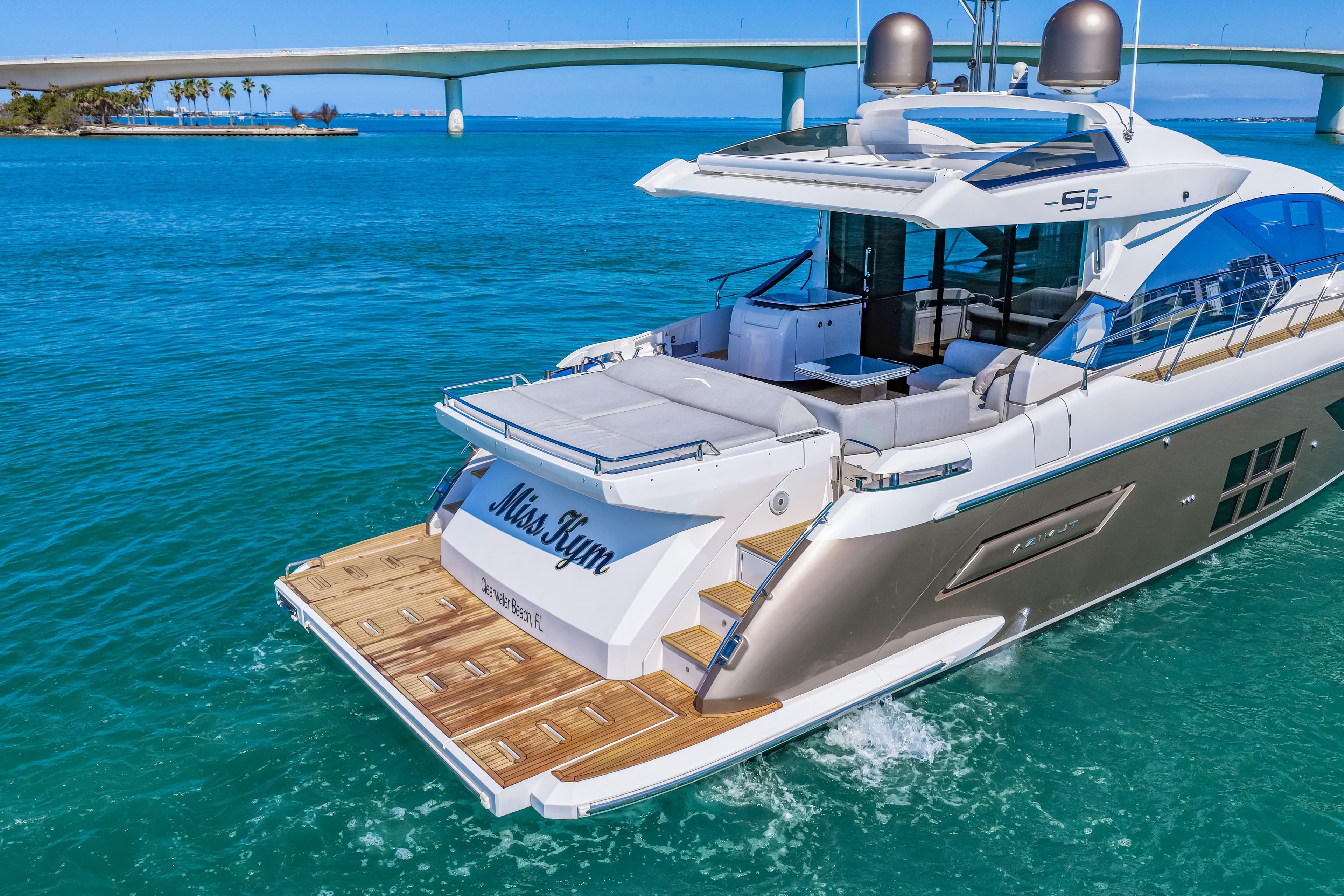 Luxury 2020 Azimut S6 yacht cruising in clear blue waters near a bridge.