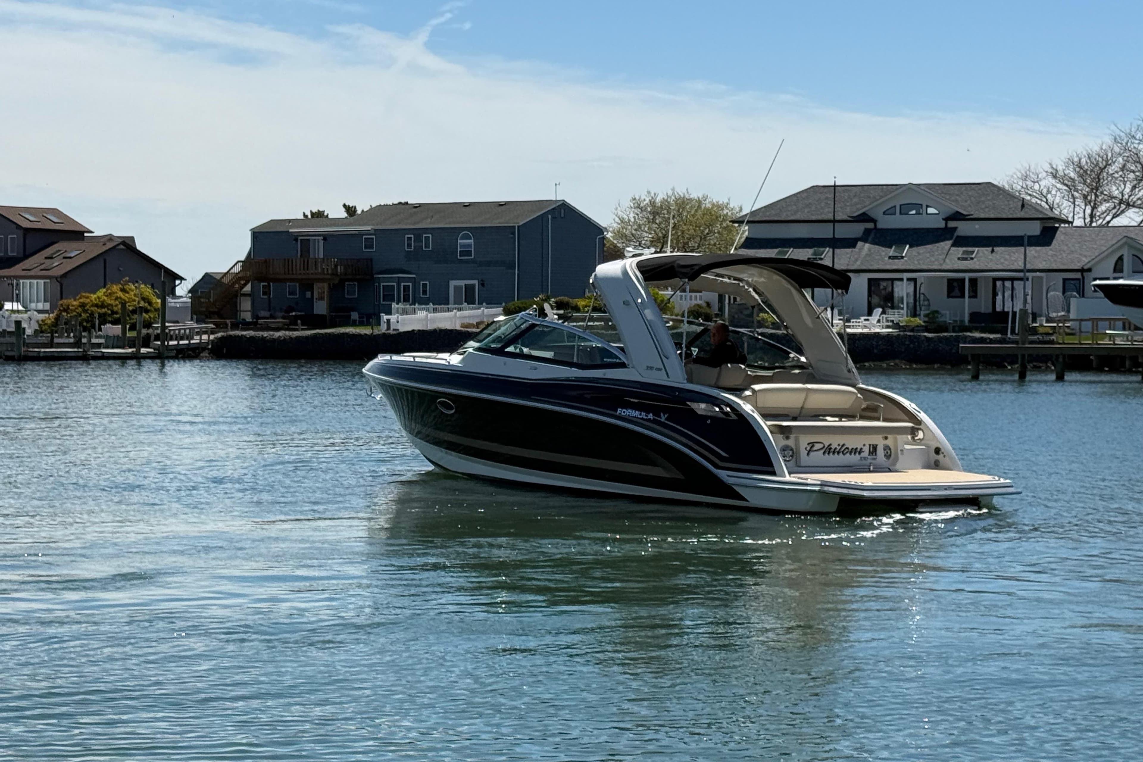 2015 Formula 330 Crossover Bowrider cruising on a calm waterfront near houses.