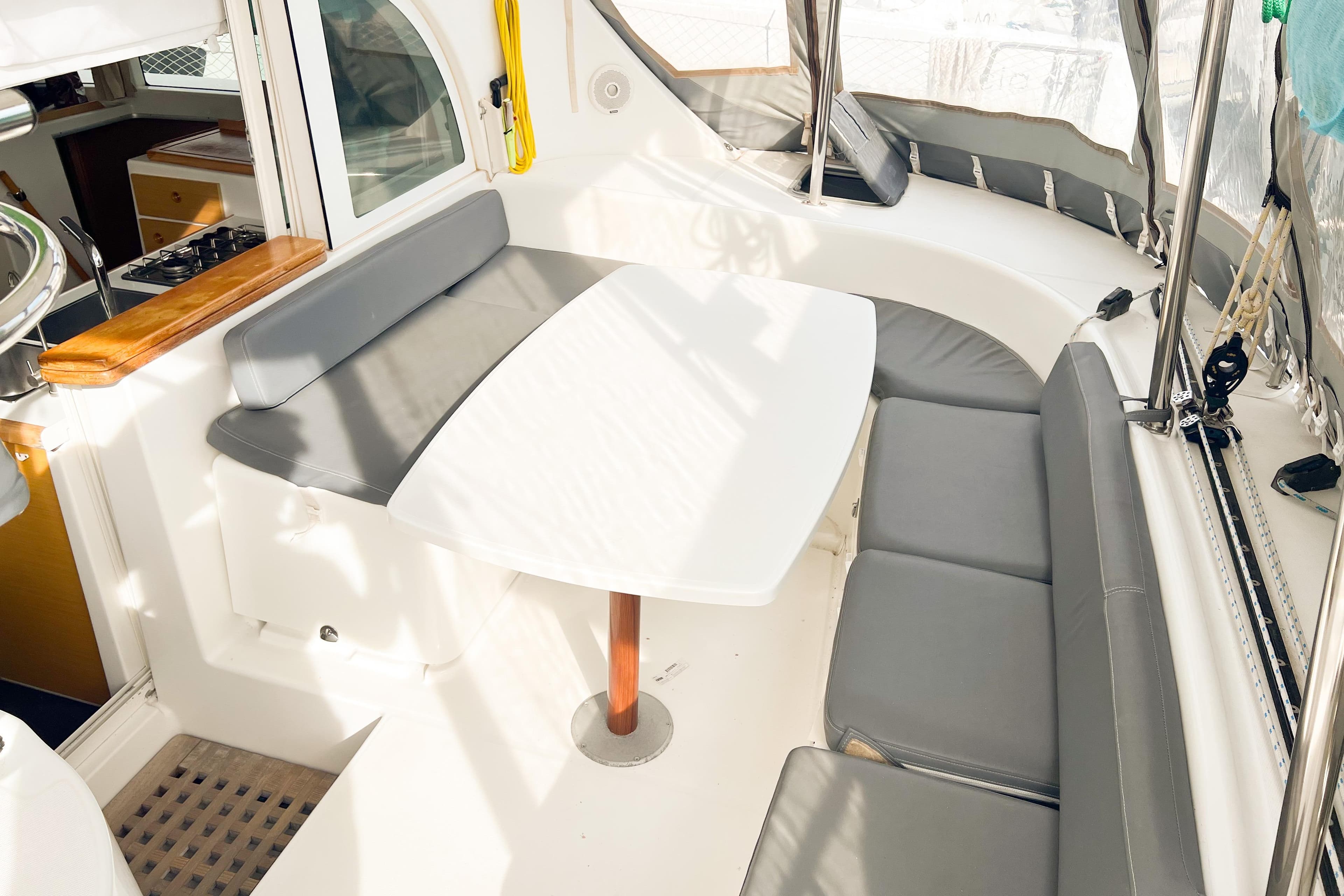 Spacious seating area on a 2008 Lagoon 380 S2 catamaran with a white table and gray cushions.