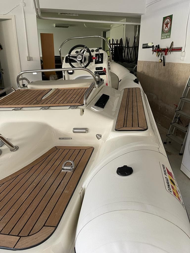 2012 Conrad Pischel boat with wooden deck, steering wheel, and sleek design in a garage setting.