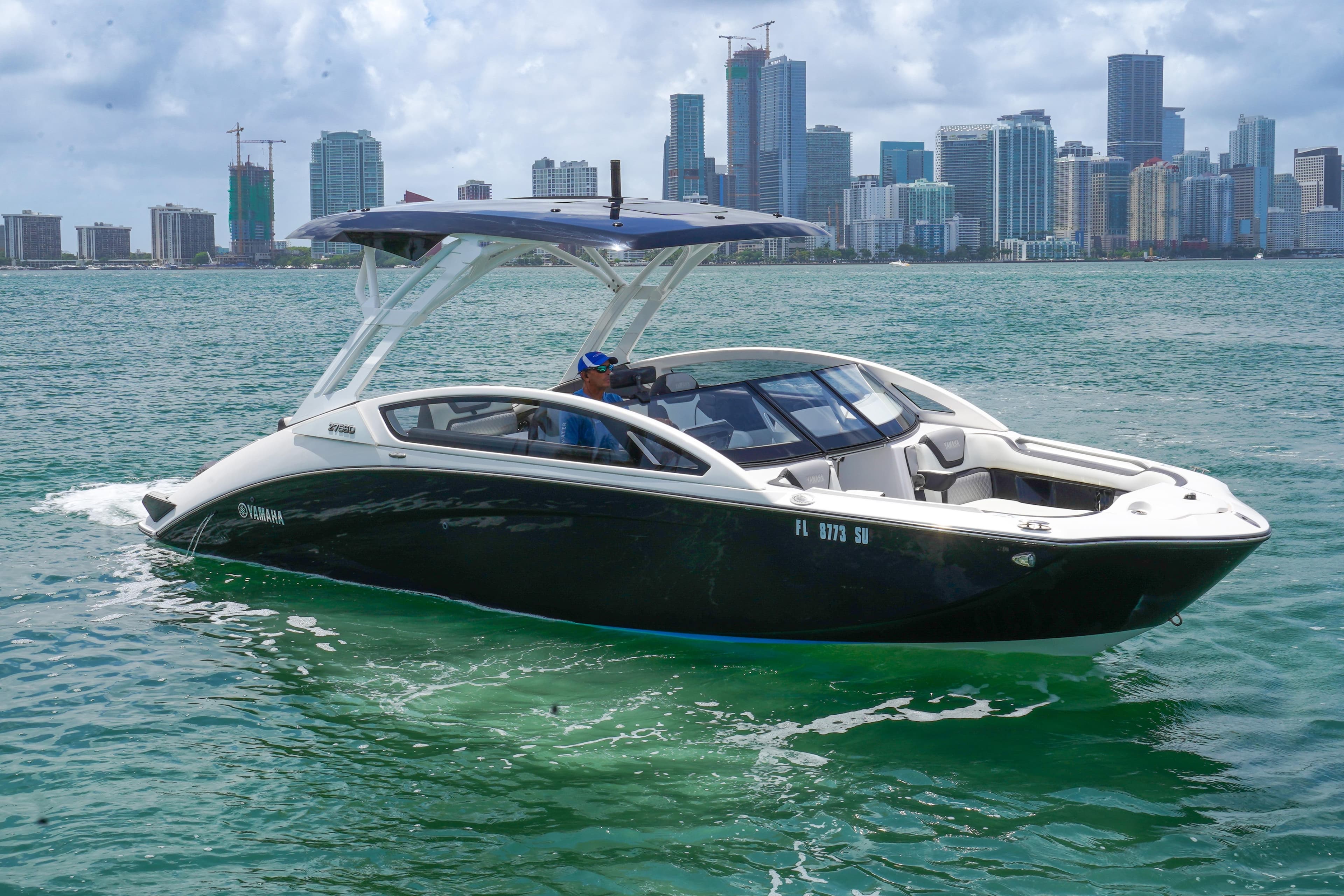 2021 Yamaha Boats 275SD cruising on water with city skyline backdrop.