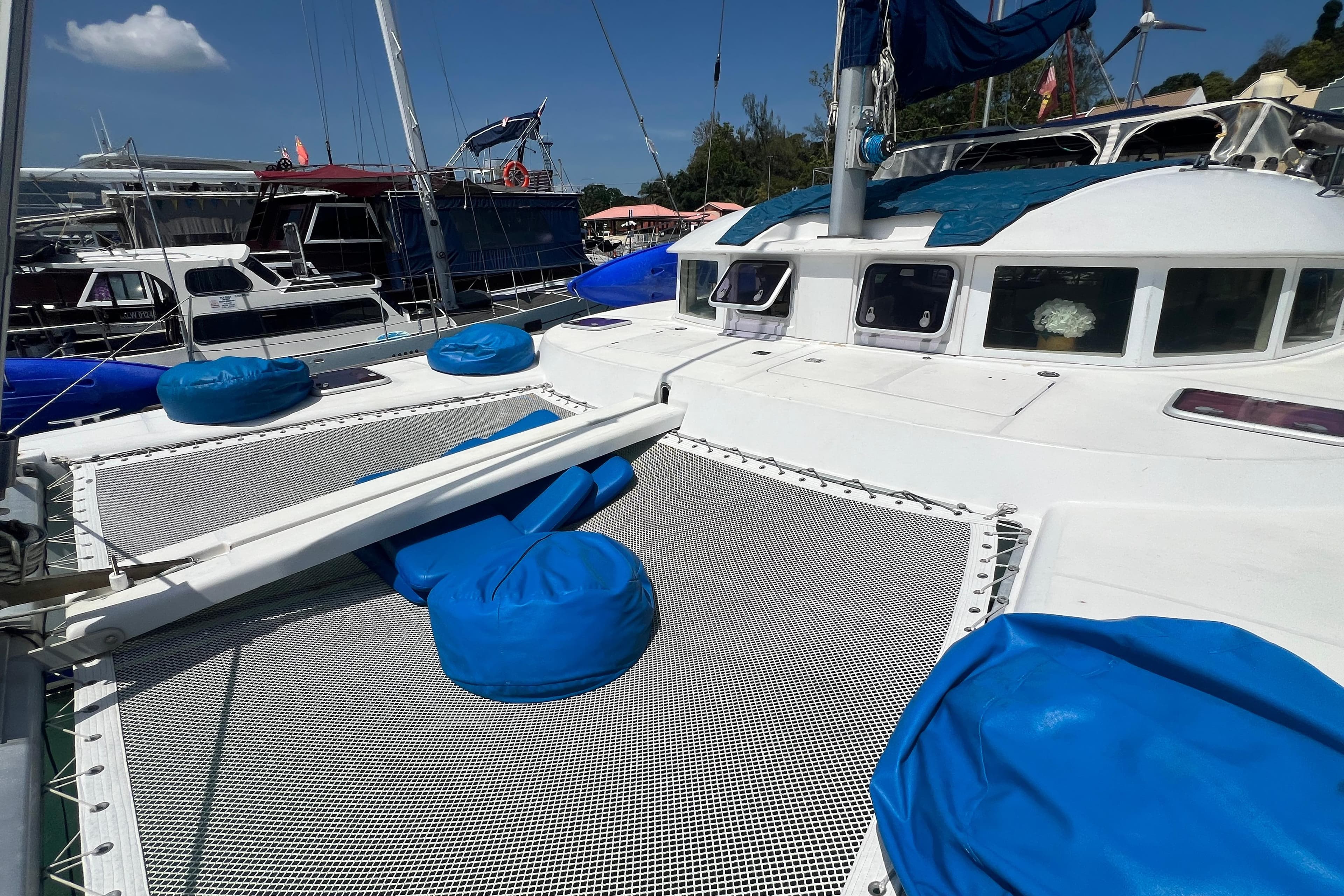 2003 Lagoon 380 catamaran with blue cushions, docked in a marina under clear skies.