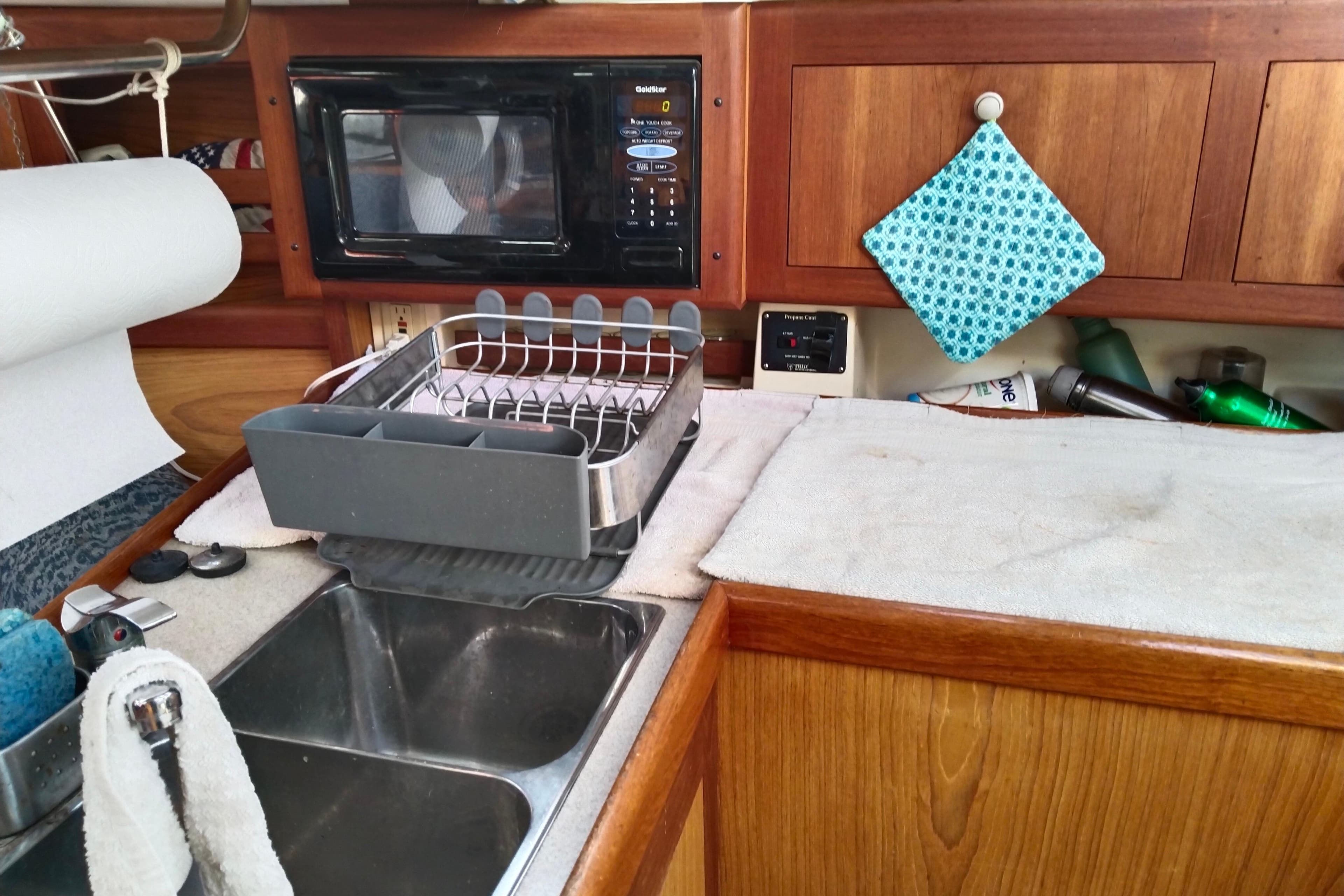 Galley kitchen in 1999 Hunter 380 sailboat with sink, microwave, and dish rack.