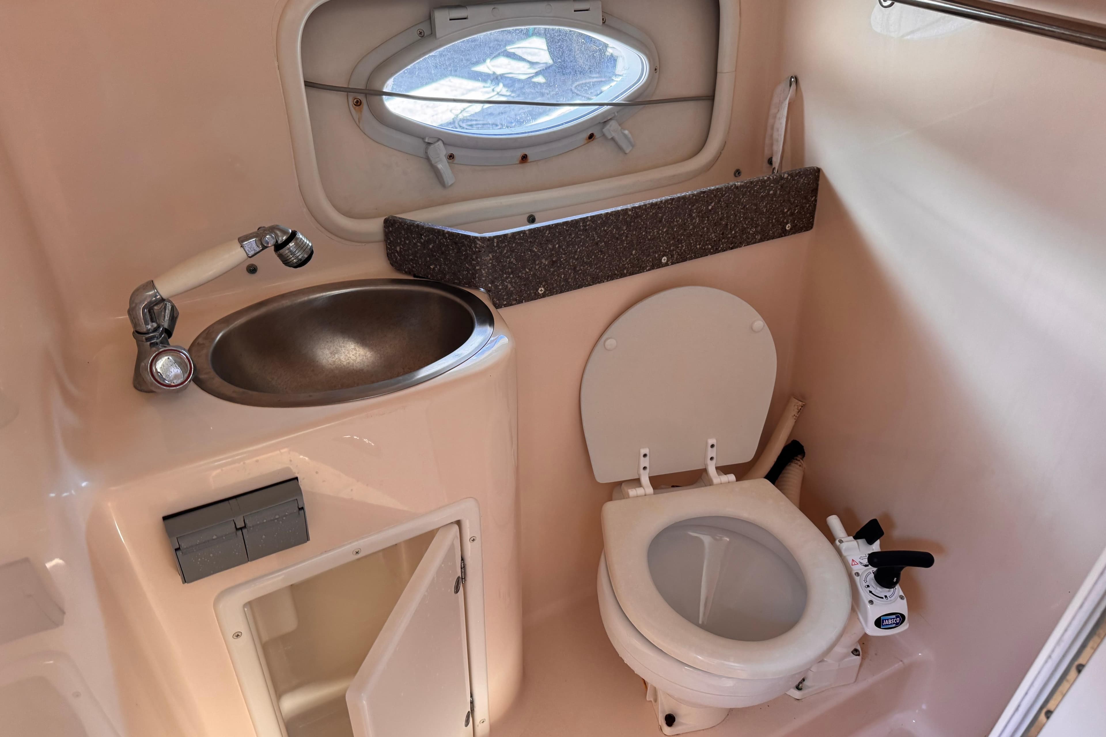 2004 Rinker Fiesta Vee 270 boat bathroom with sink, toilet, and porthole window.