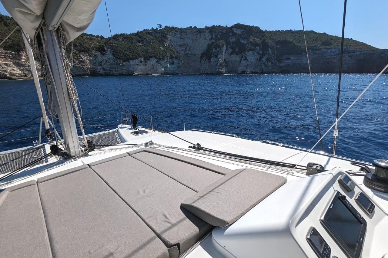 Lagoon 450 F Owners Version 2014 sailing near rocky coastline under clear blue sky.