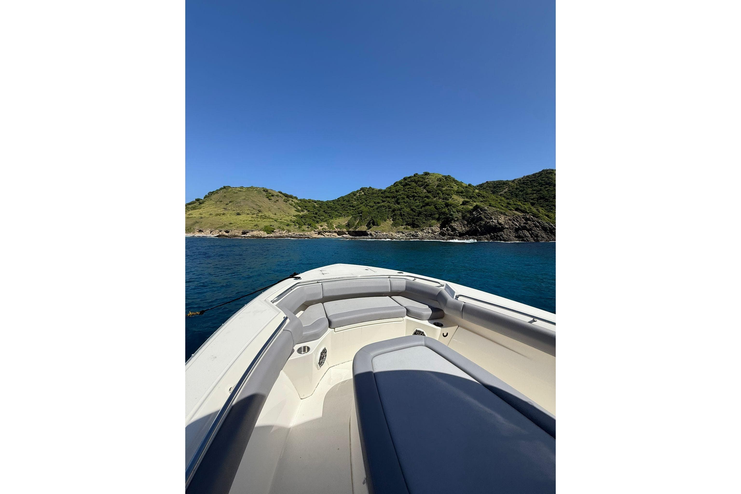 2024 Boston Whaler 280 Outrage cruising near lush green island under clear blue sky.