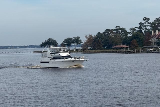 1990 Californian 45 Motor Yacht cruising on a calm lake near a wooded shoreline.