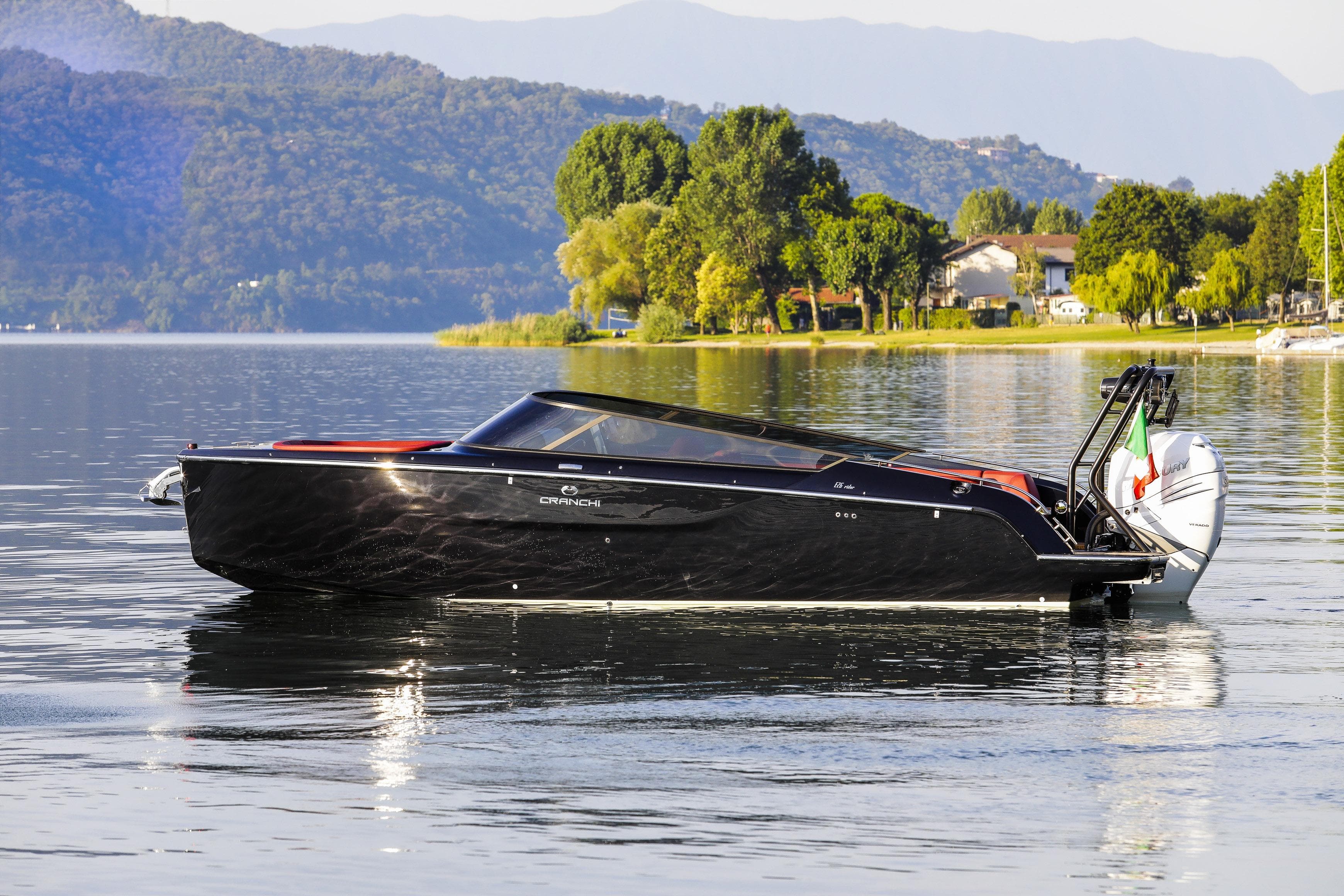 2026 Cranchi E26 Rider boat on a serene lake with scenic mountain backdrop.