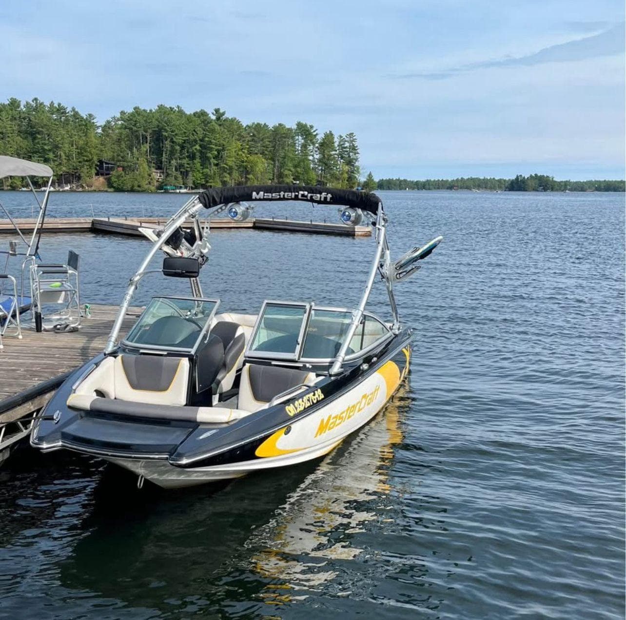 2011 MasterCraft X2 boat docked on a serene lake with lush forest background.