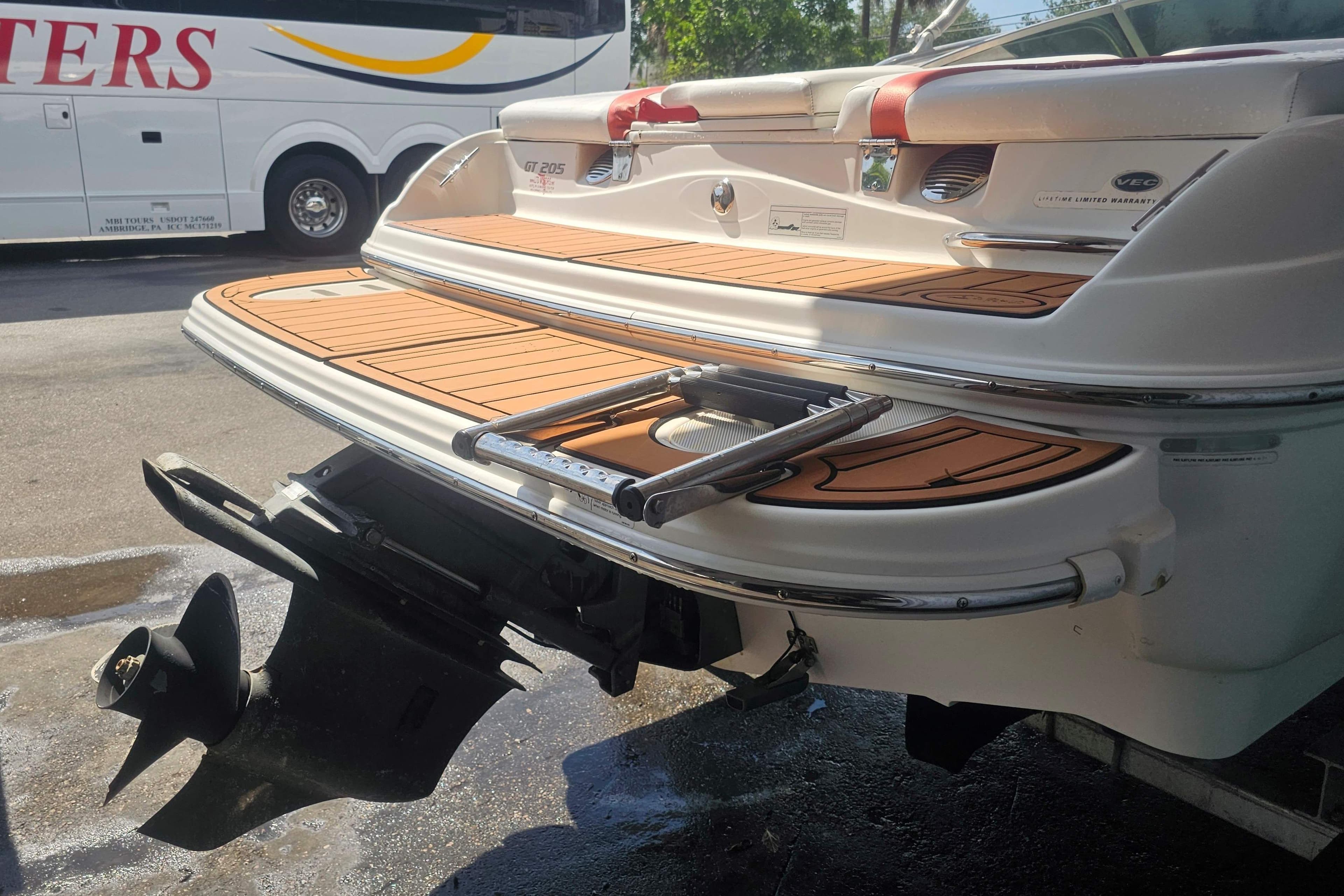 2008 Glastron GT 205 boat stern with swim platform and ladder, parked near a bus.