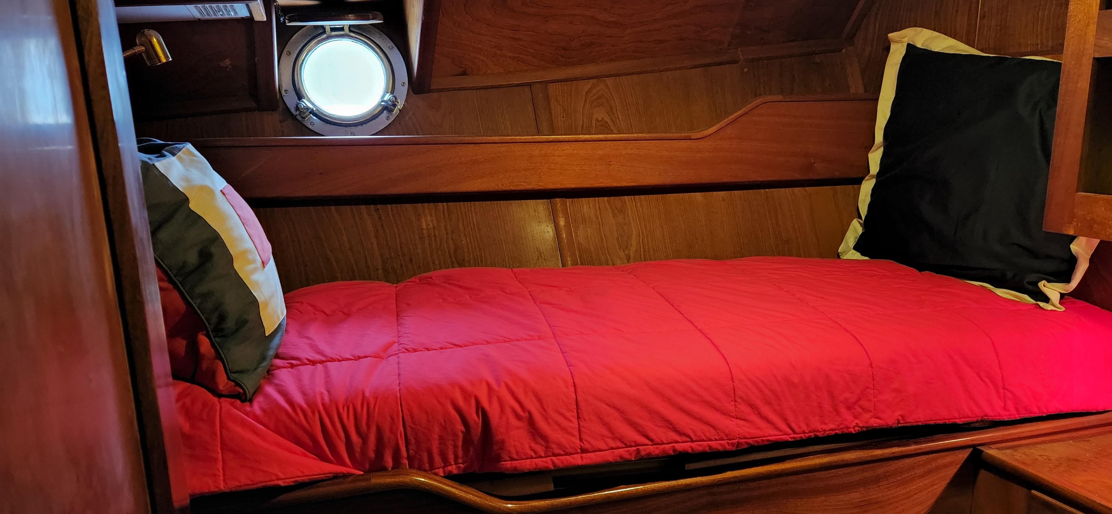 Cozy cabin bed in 1983 Thackwray Custom Pilothouse Motorsailer with red bedding and porthole.