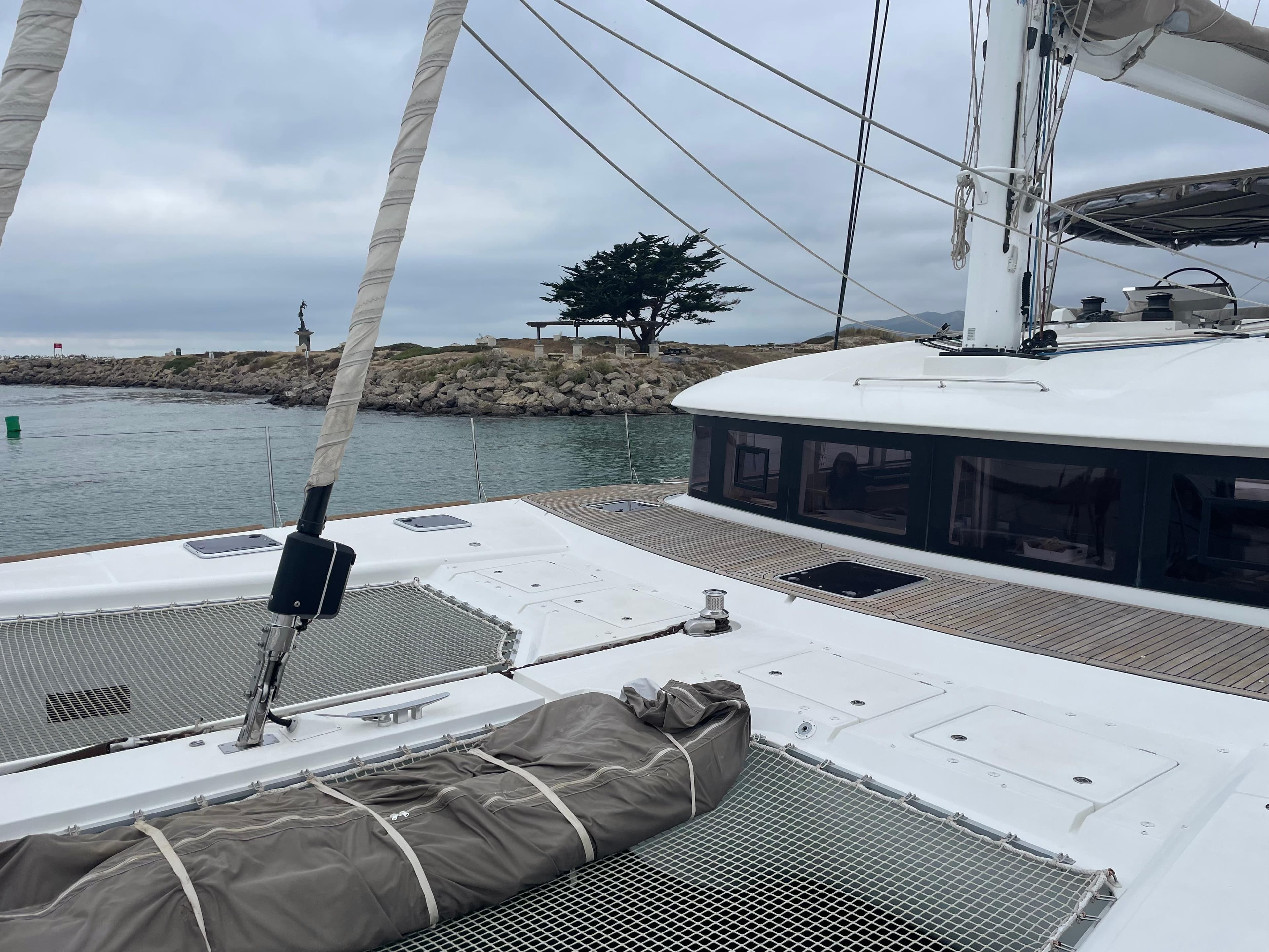 Lagoon 620 catamaran sailing near rocky shore, overcast sky, 2019 model.