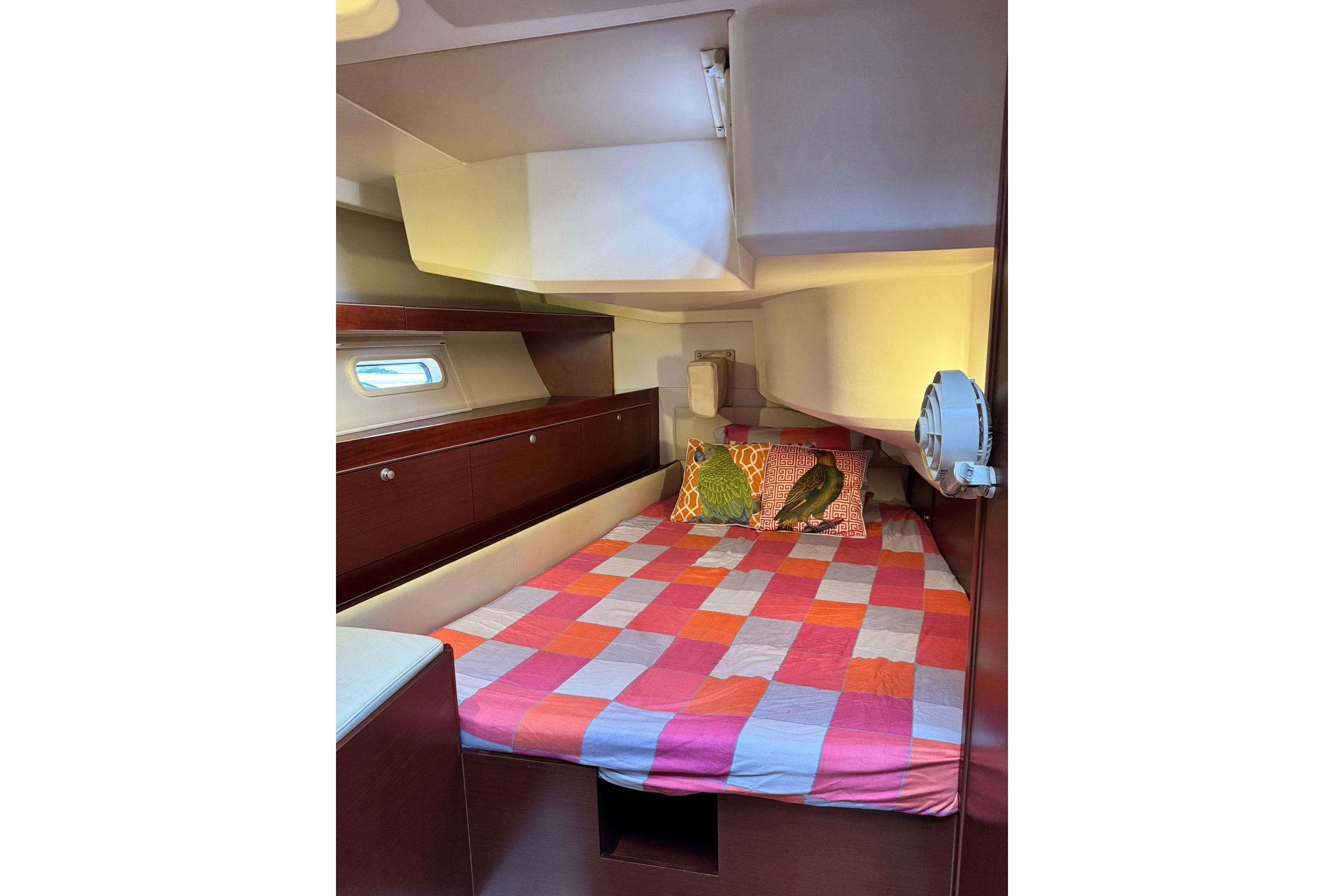 Cozy cabin interior of 2014 Hanse 575 yacht with colorful bedding and porthole.