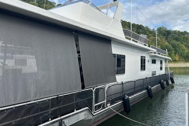 1987 Somerset Houseboat 14X60 on water, featuring shaded windows and railing.