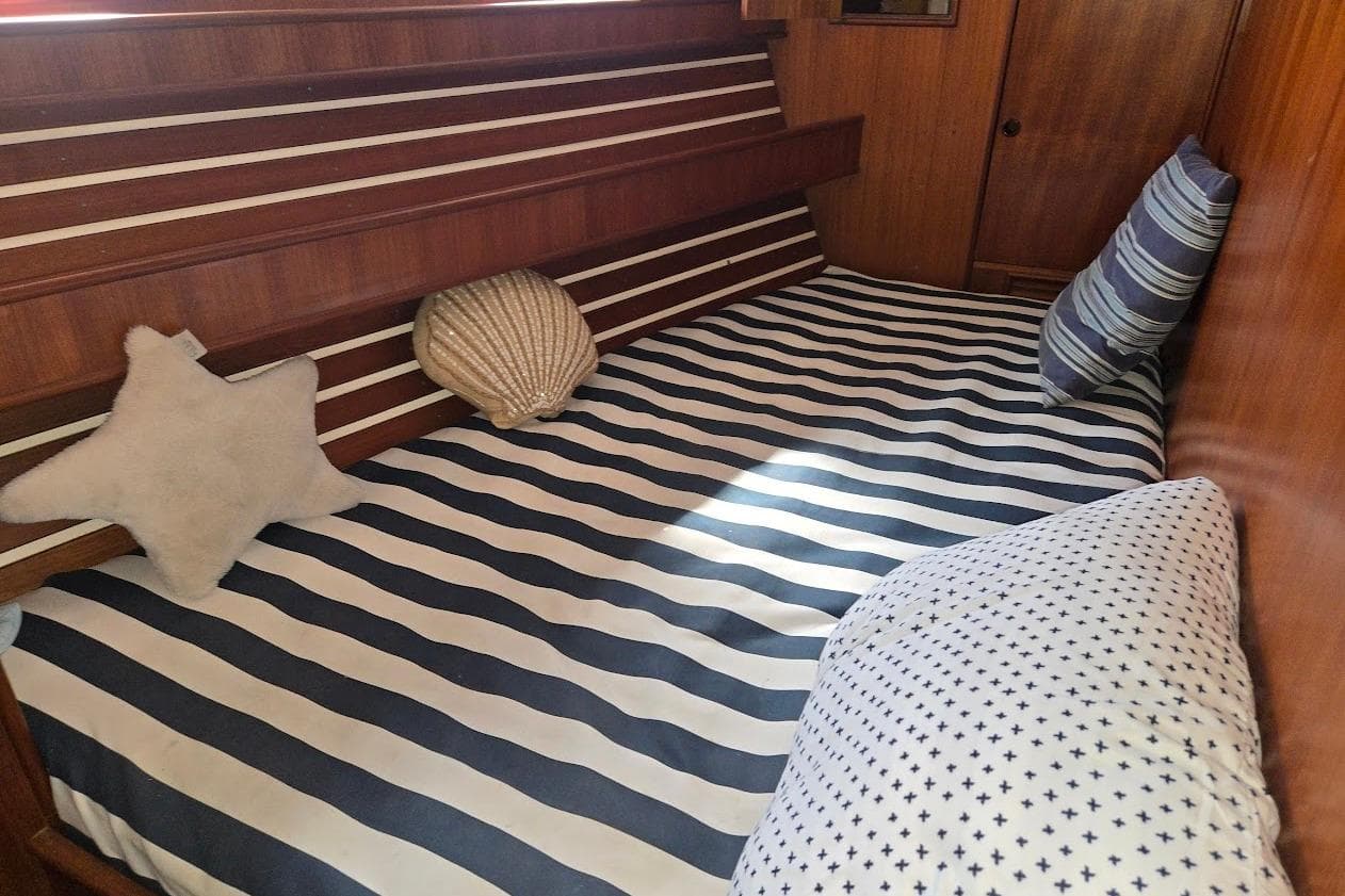 Cozy cabin interior of 1982 Tayana Center Cockpit Cutter Ketch with striped bedding and nautical decor.