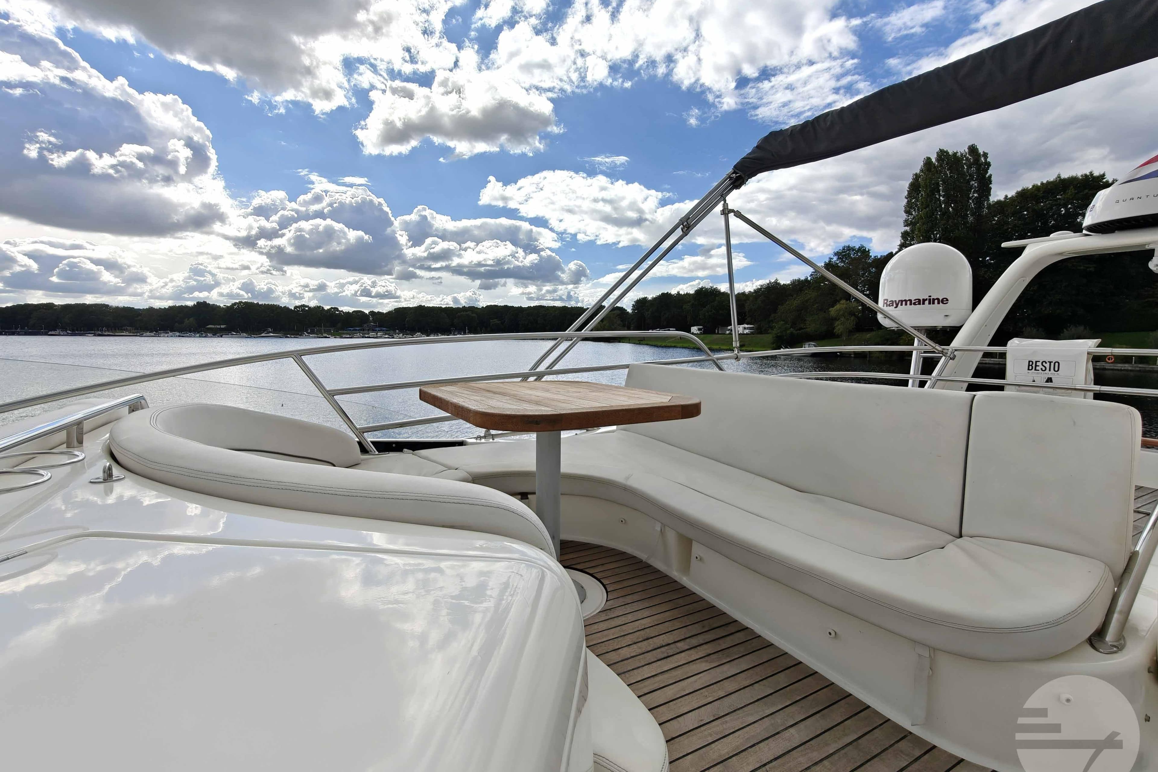 Luxurious 2006 Jeanneau Prestige 46 yacht deck with seating and table, under a partly cloudy sky.