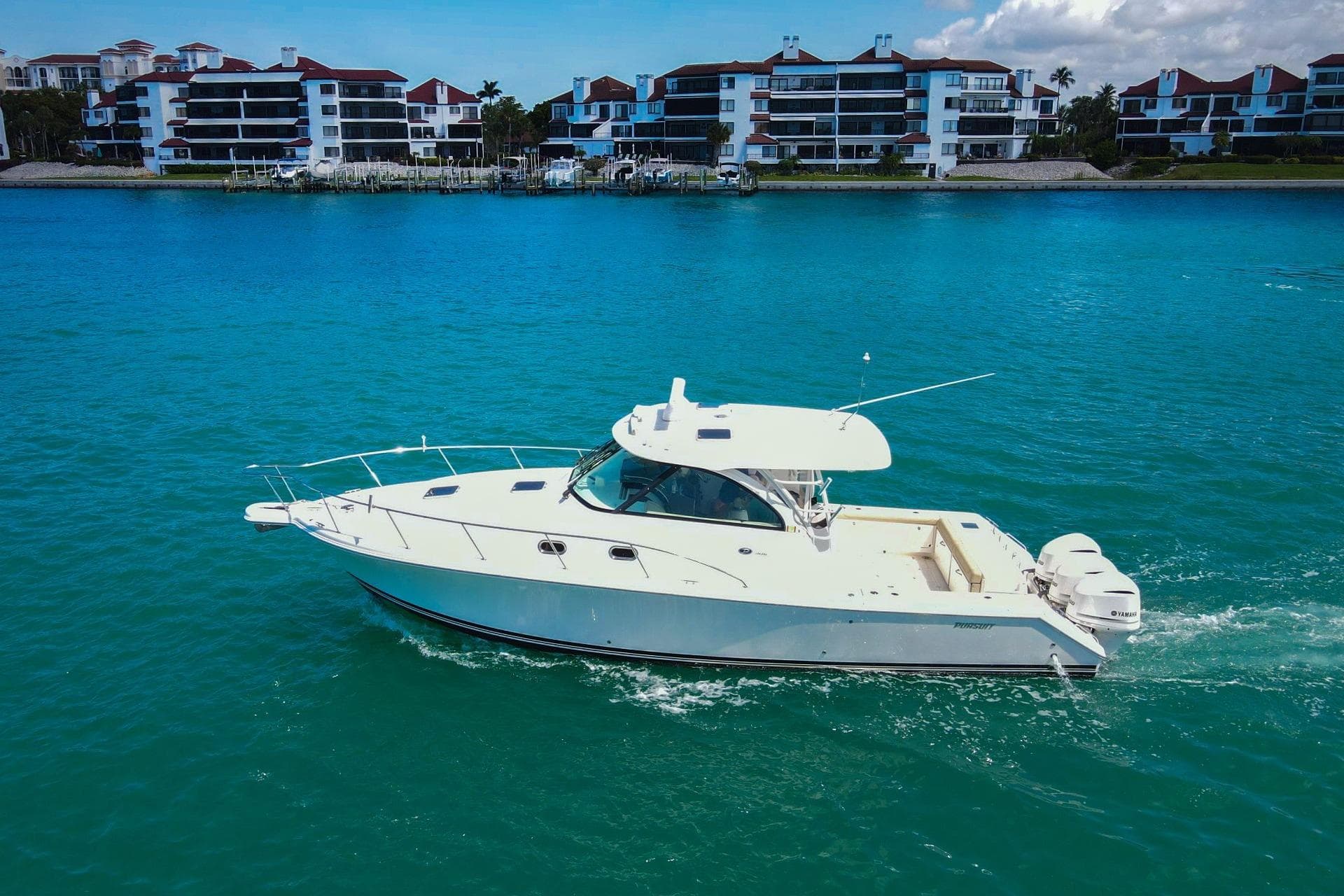 2019 Pursuit OS 385 Offshore boat cruising on turquoise water near waterfront buildings.