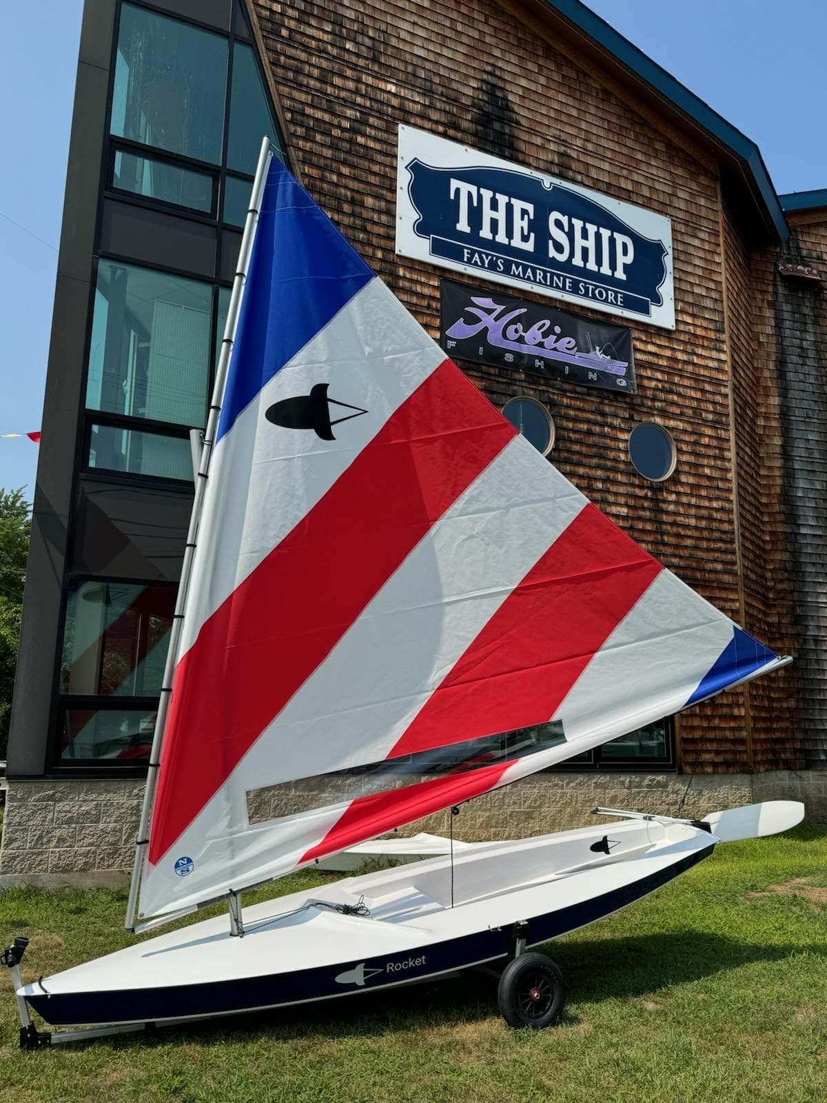 2025 Dinghy Rocket Board Boat with colorful sail outside marine store.