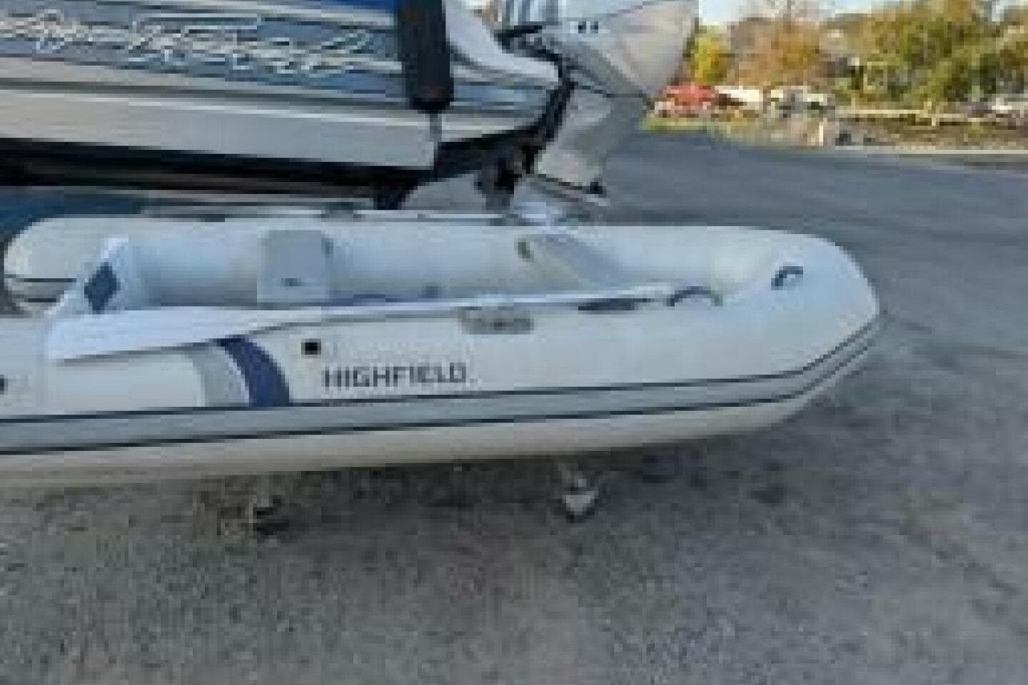 White inflatable Highfield boat on a trailer, parked outdoors near a larger vessel.