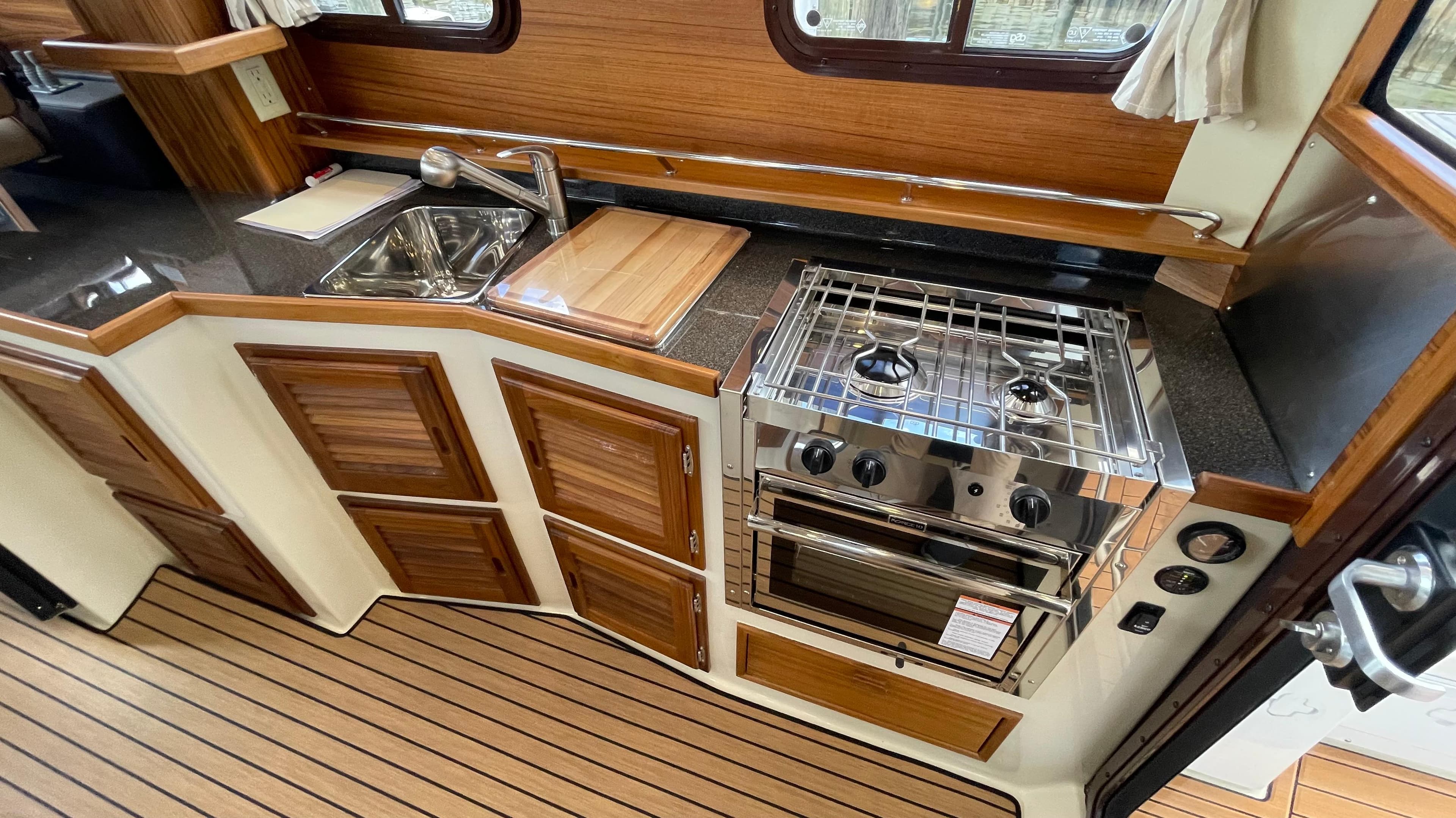 2023 Ranger Tugs R-31 CB kitchen with stove, sink, and wooden cabinetry.