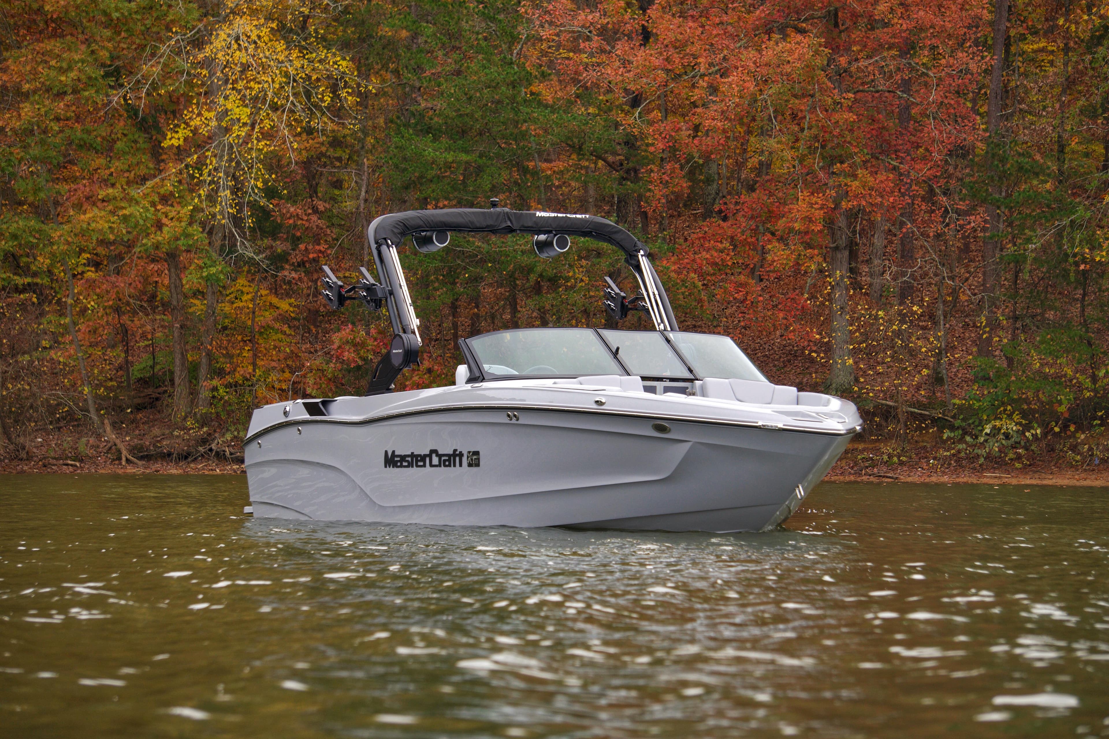 2025 MasterCraft XT23 boat on a lake with autumn foliage background.