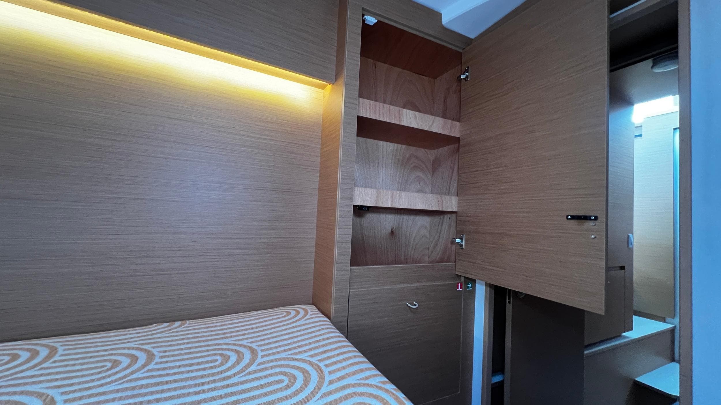 Modern cabin interior with wooden storage, ambient lighting, and patterned bedding in Excess 11, 2023 model.