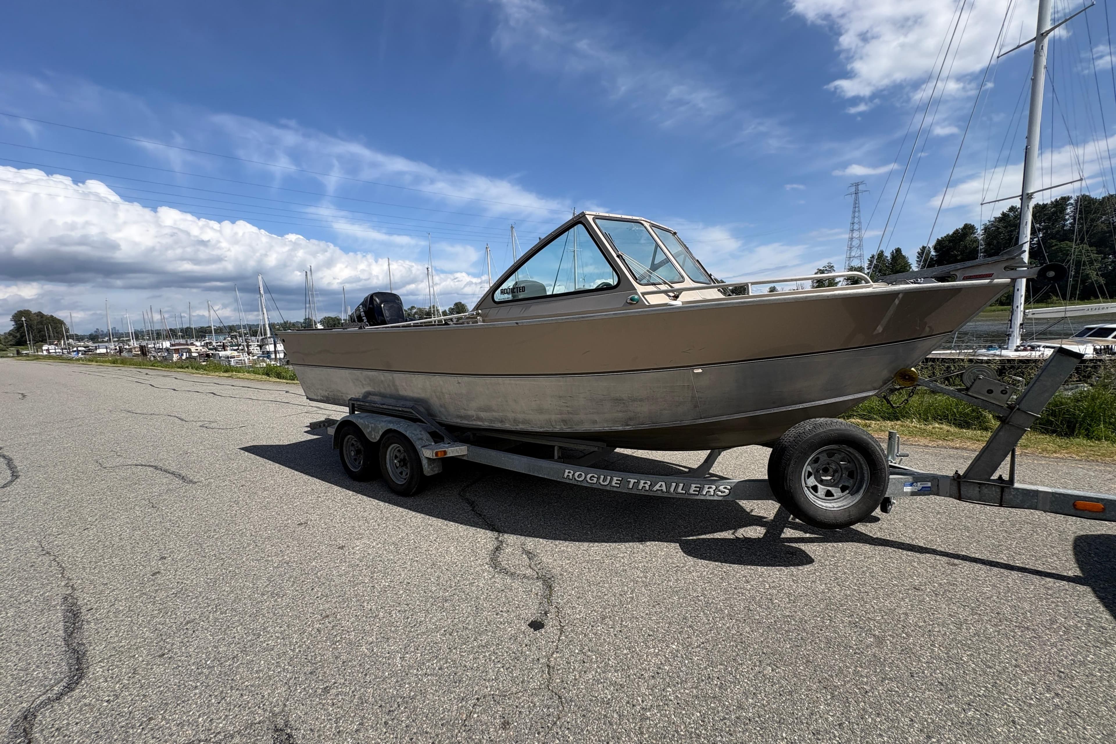 2009 Alumaweld Intruder Outboard 22 boat on trailer, parked near marina under blue sky.