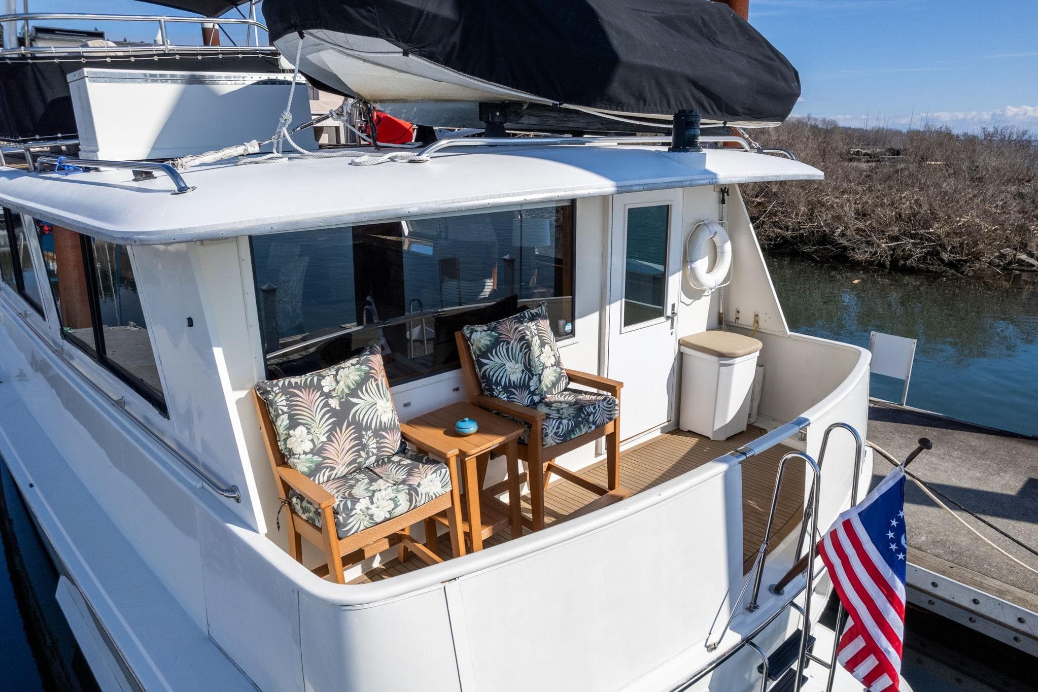 1986 Hatteras 63 Motor Yacht with deck seating and American flag, docked by water.