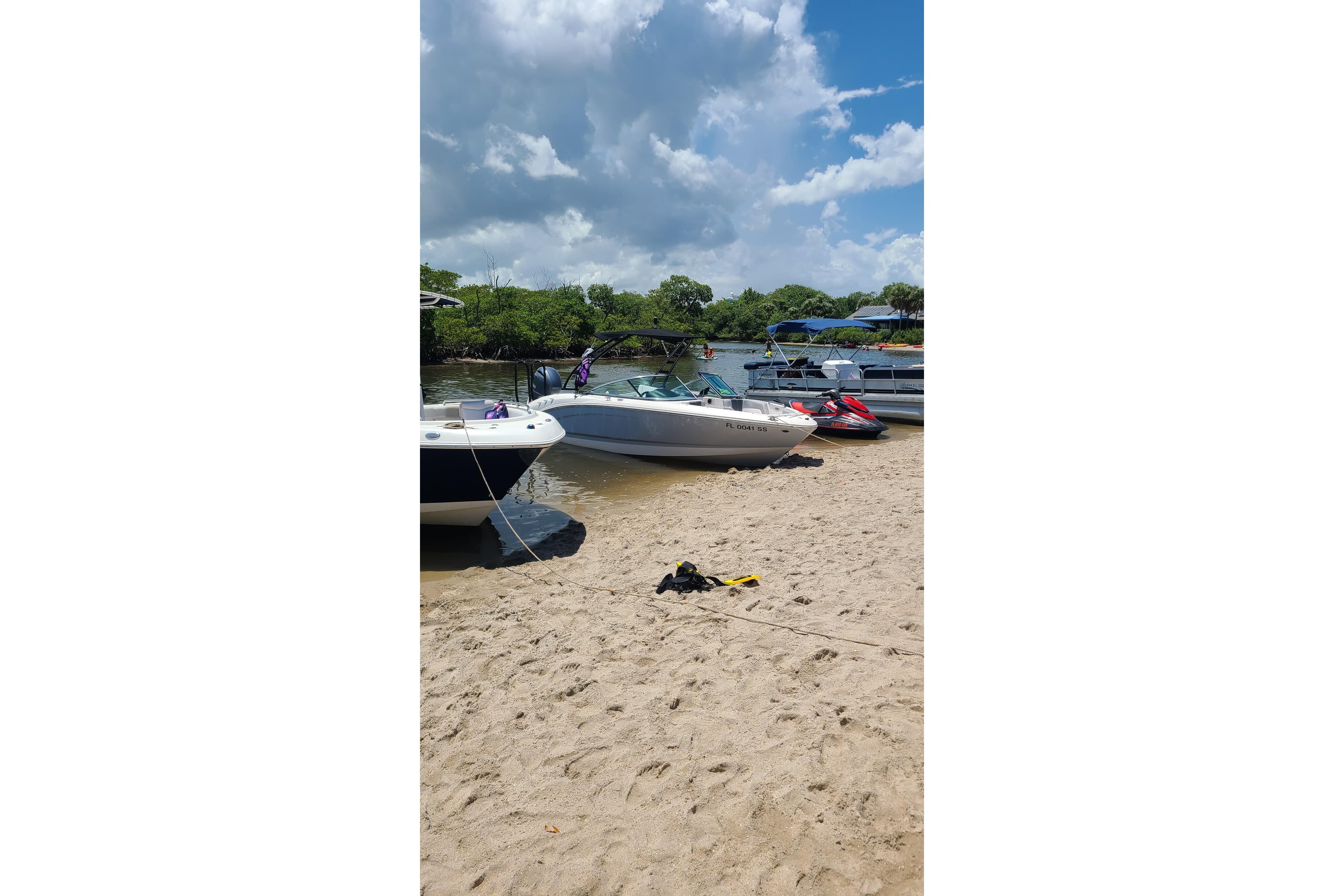 Boats and jet skis on a sandy shore under a cloudy sky, featuring a 2020 Chaparral 21 SSi OB.