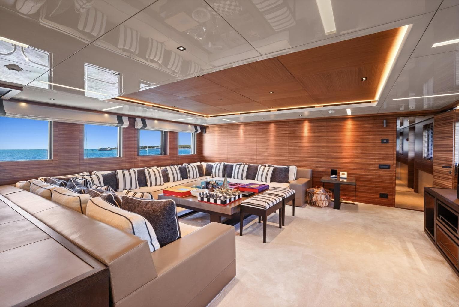 Luxurious yacht interior with striped cushions, wooden paneling, and ocean view through large windows.
