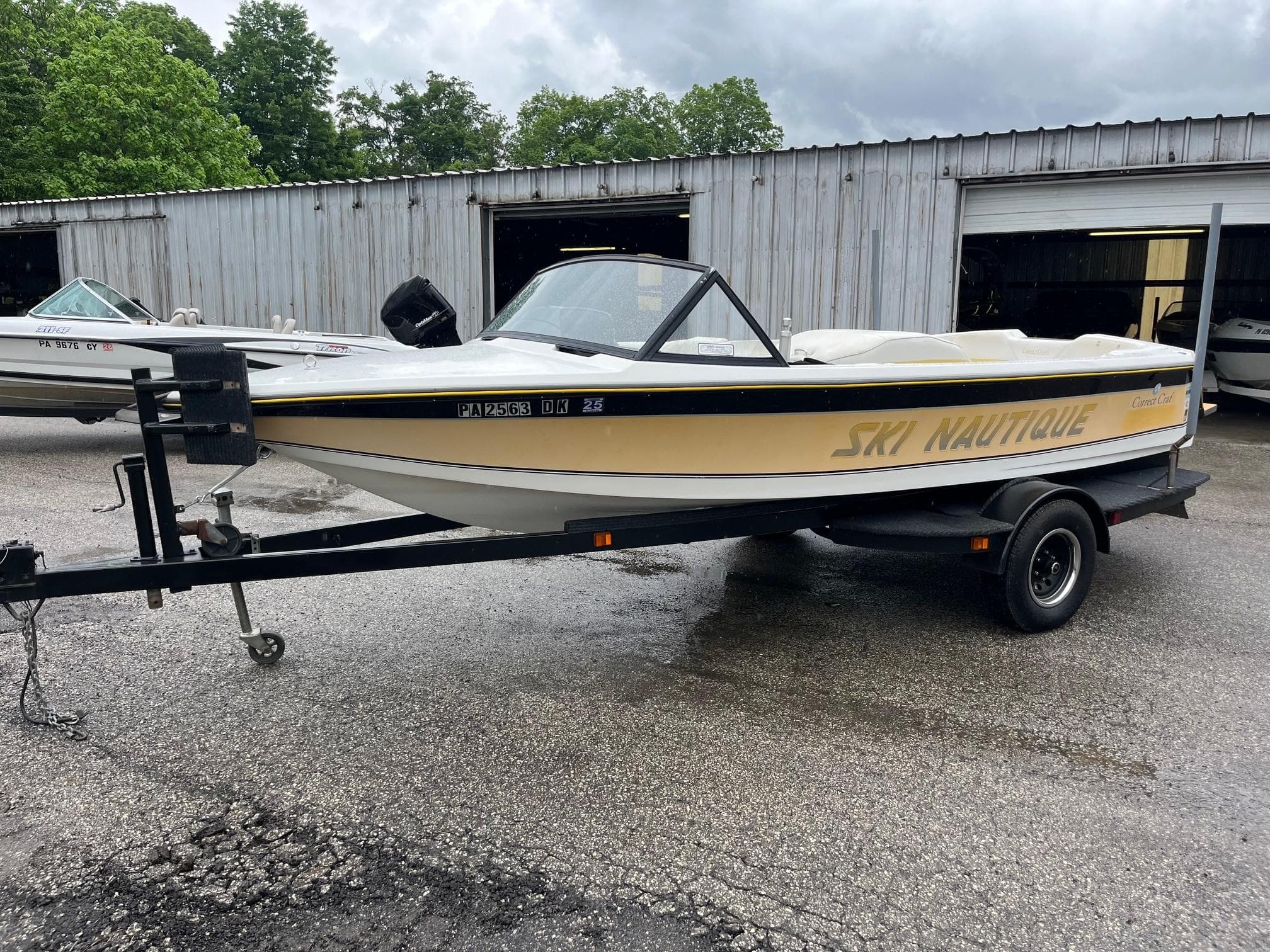 1990 Correct Craft Ski Nautique boat on trailer, parked outdoors near a garage.