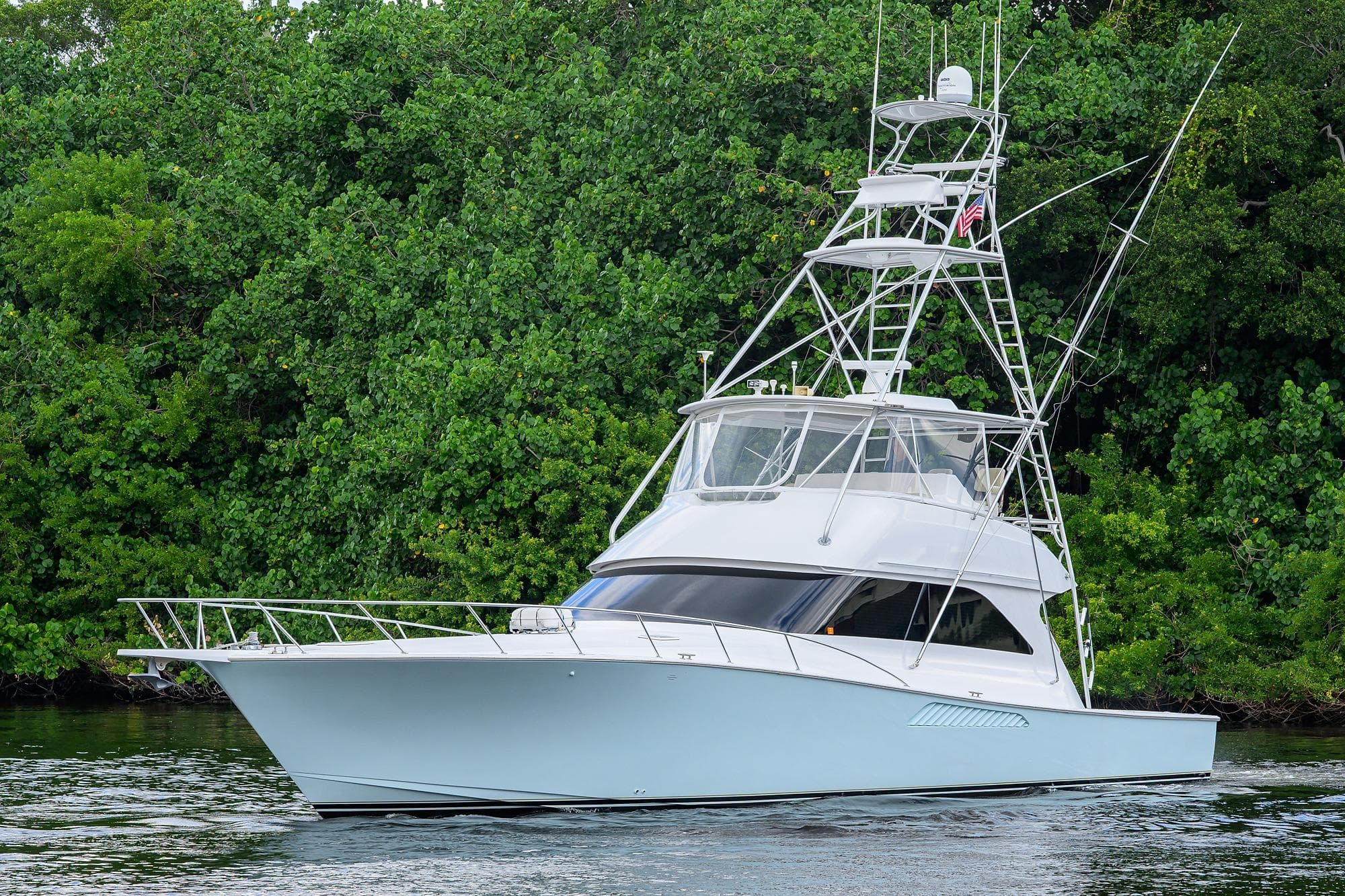 2004 Viking 56 Convertible yacht cruising near lush green shoreline.
