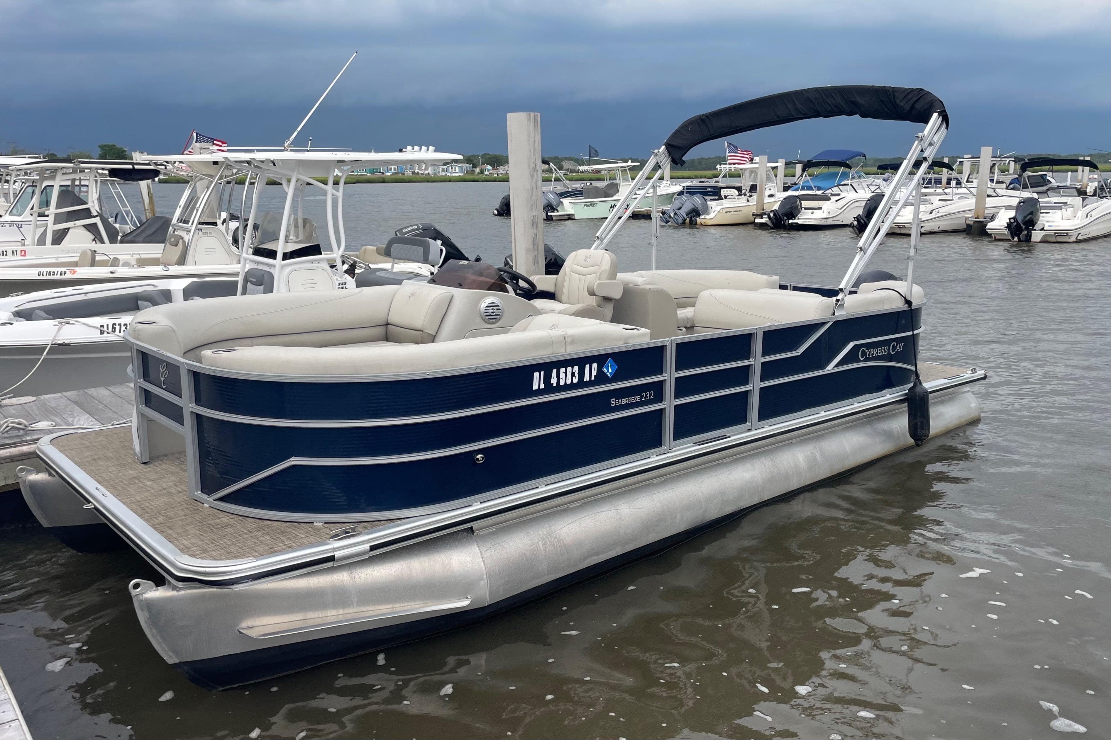 2023 Cypress Cay Seabreeze 232 pontoon boat docked in a marina, overcast sky.