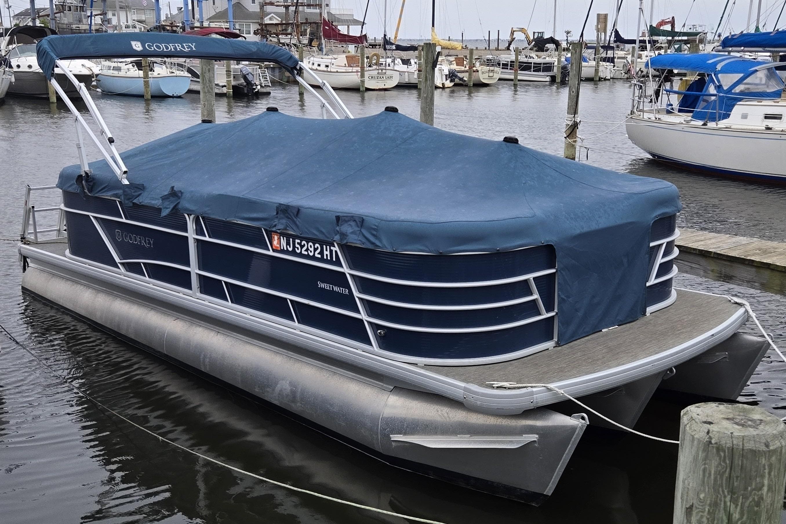 2023 Godfrey Sweetwater 2286 SBX pontoon boat docked with cover in marina.