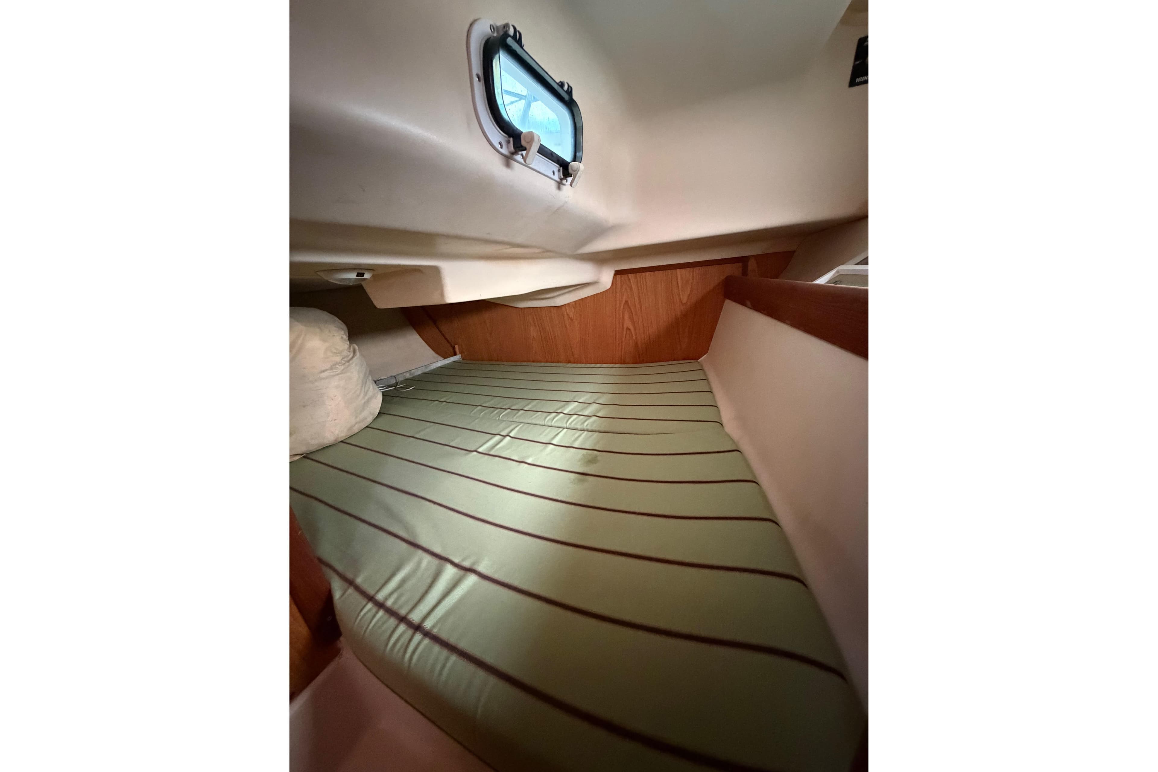 Cozy cabin interior of 2000 Hunter 310 sailboat with striped mattress and porthole.