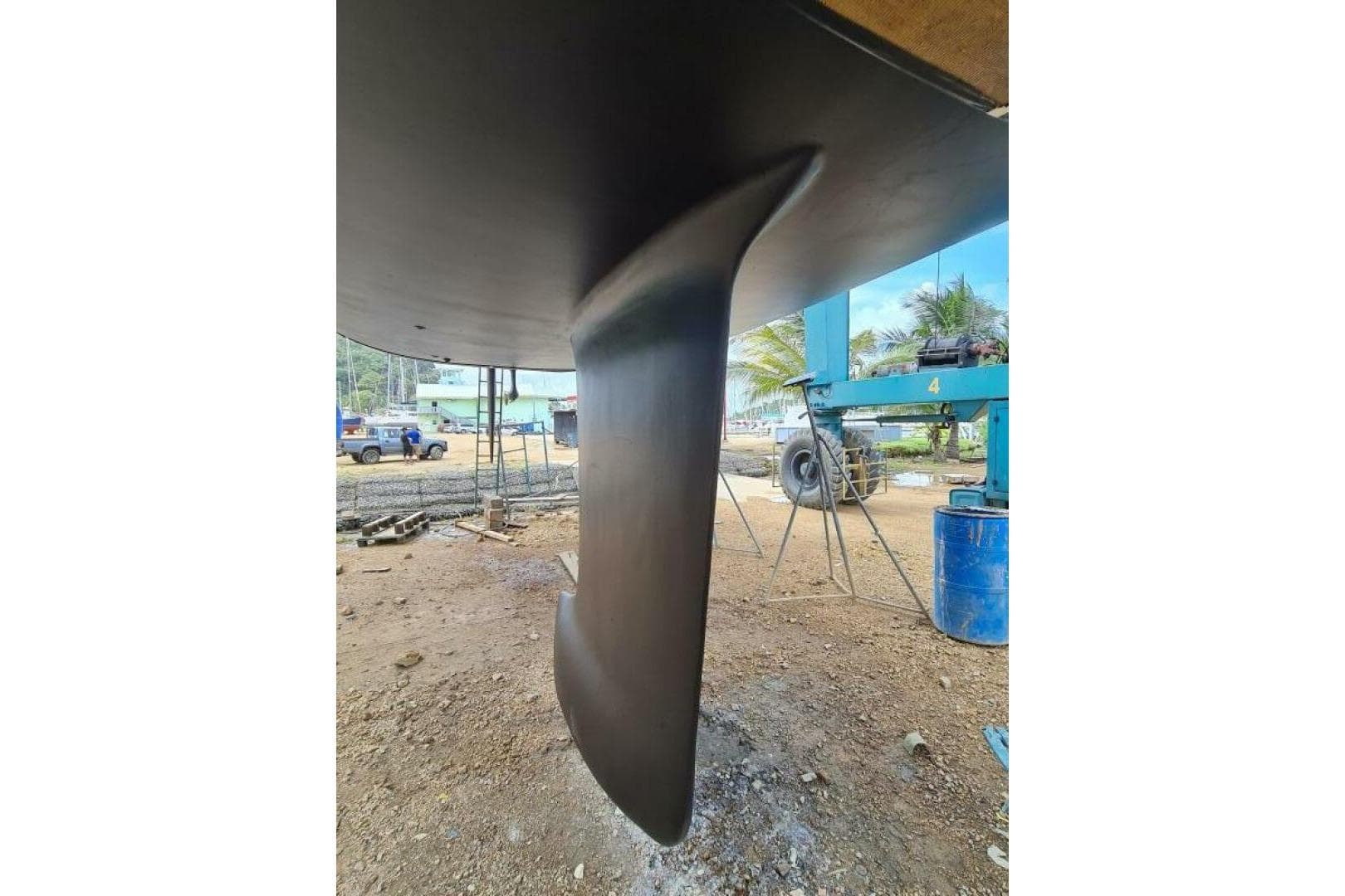 Hanse 470e 2010 yacht keel in a shipyard, with equipment and palm trees in the background.