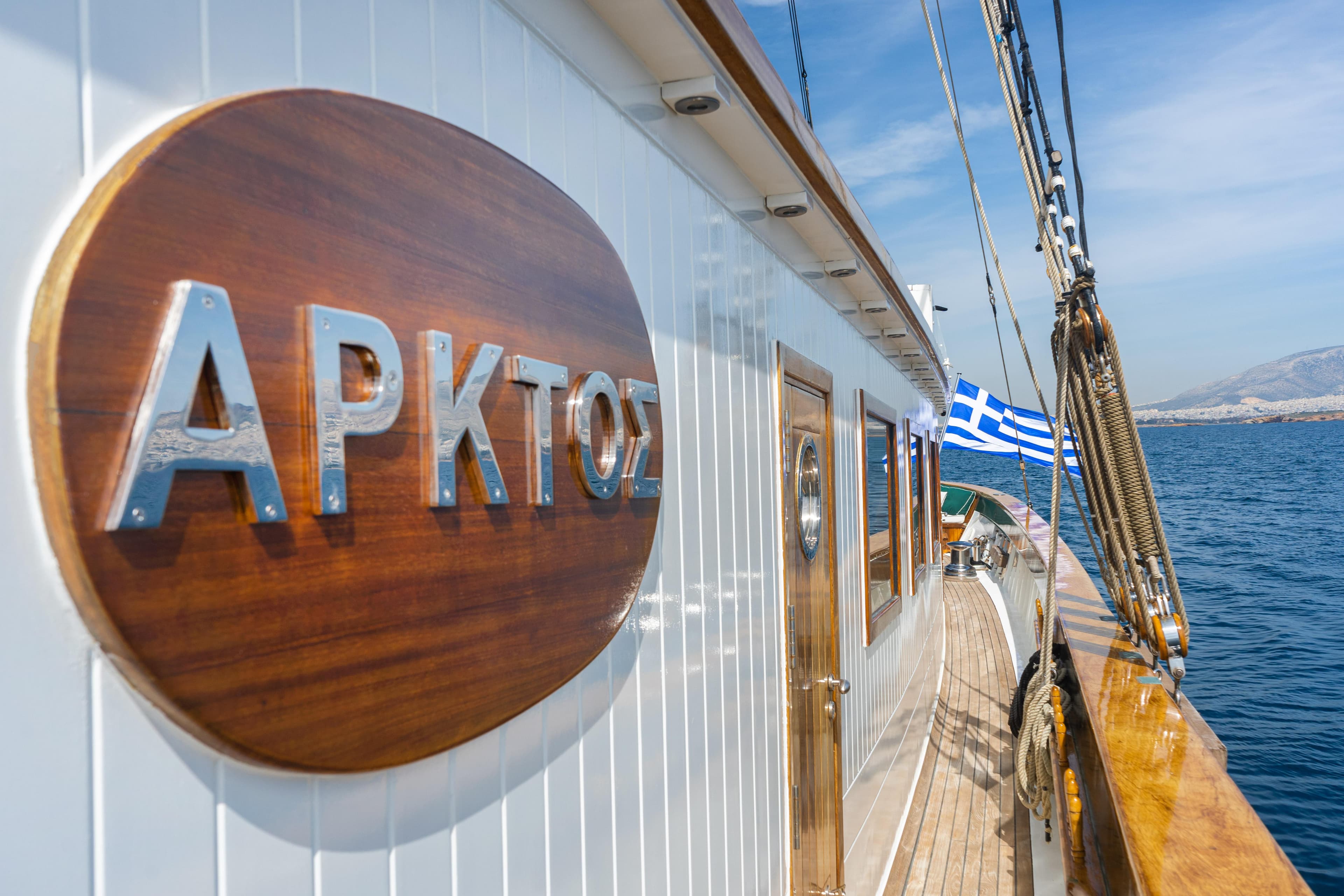 Wooden yacht with Greek flag and "ARKTOS" sign, sailing on a sunny day, 2004 custom model.