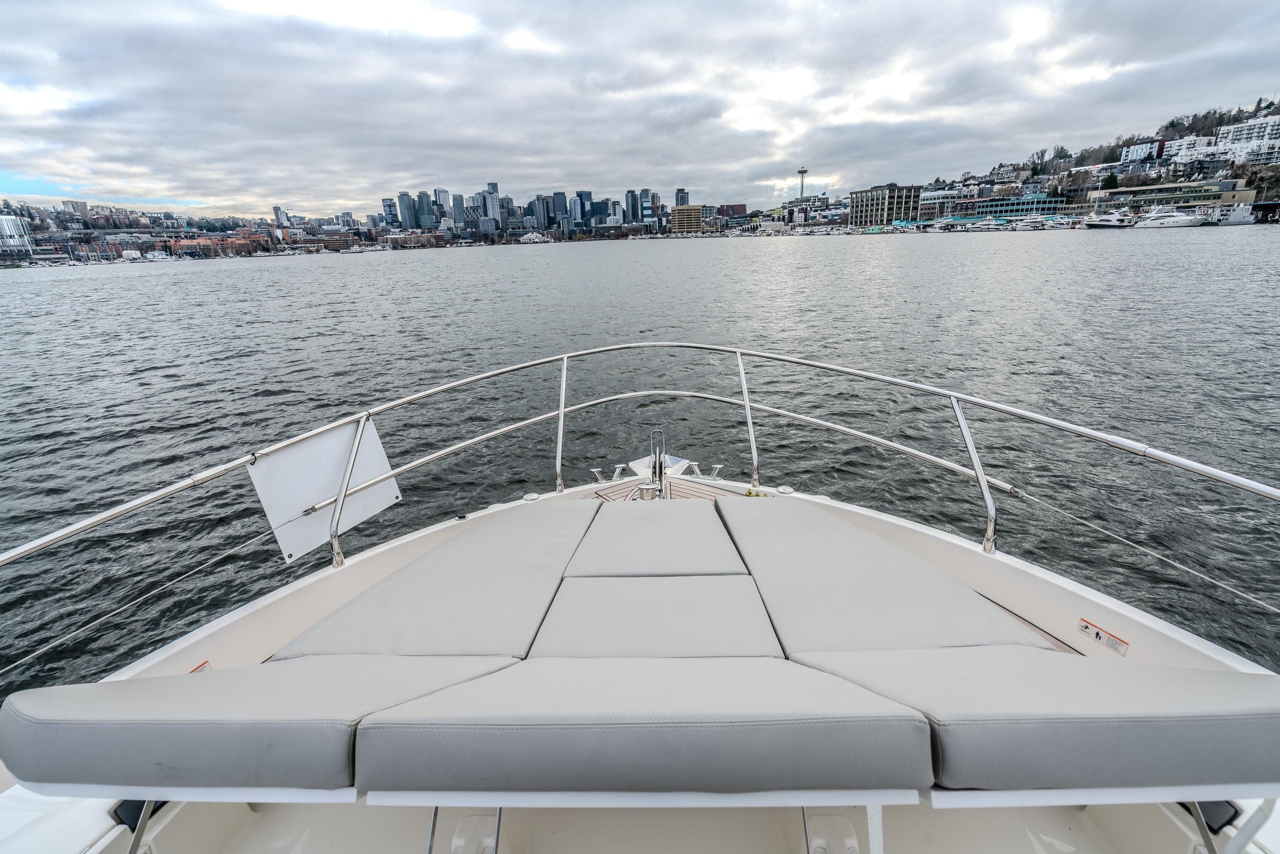 Bow view of 2026 Absolute 48 Coupe yacht approaching city skyline under cloudy skies.