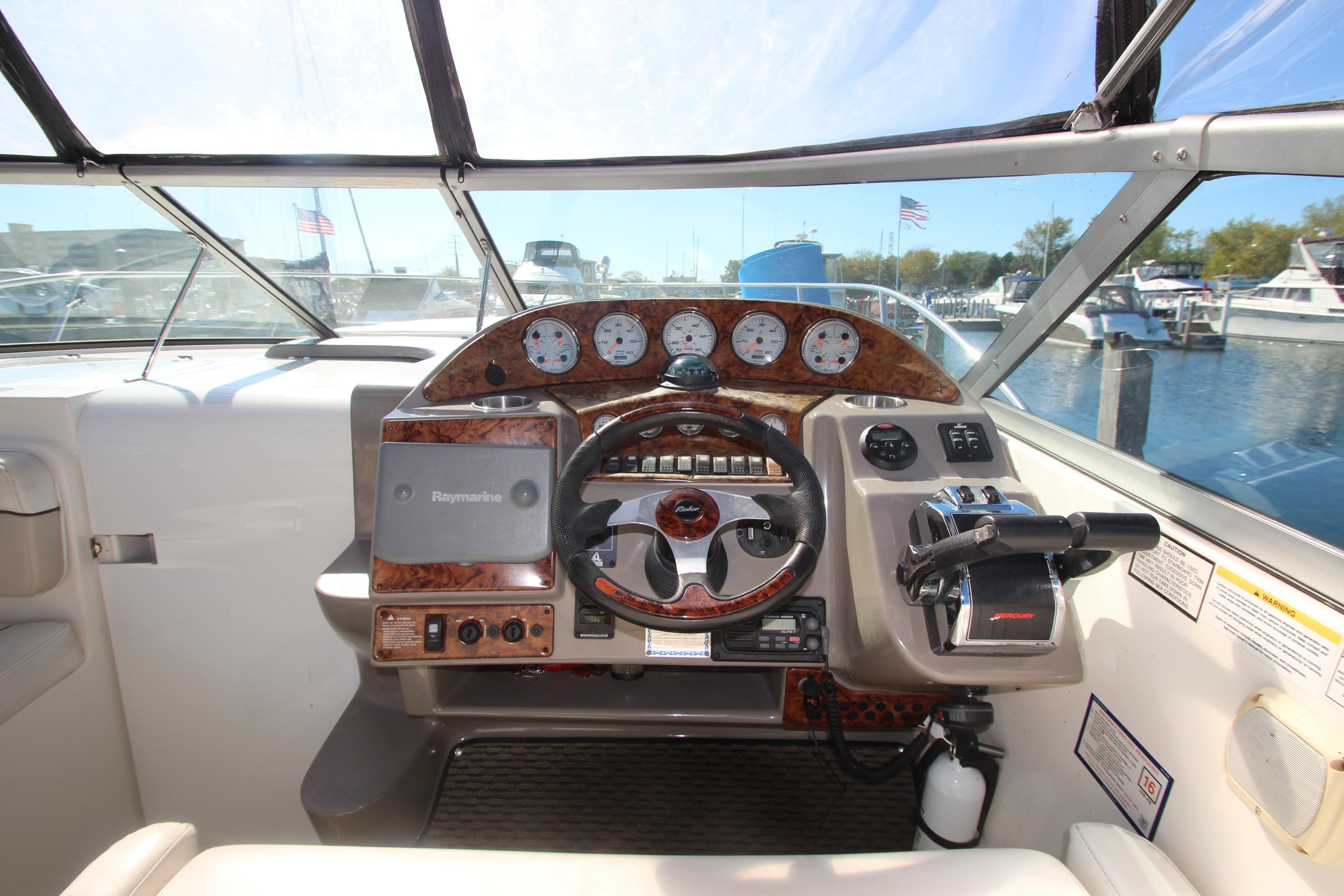 2006 Rinker 320 Express Cruiser helm with steering wheel and control panel, docked at marina.