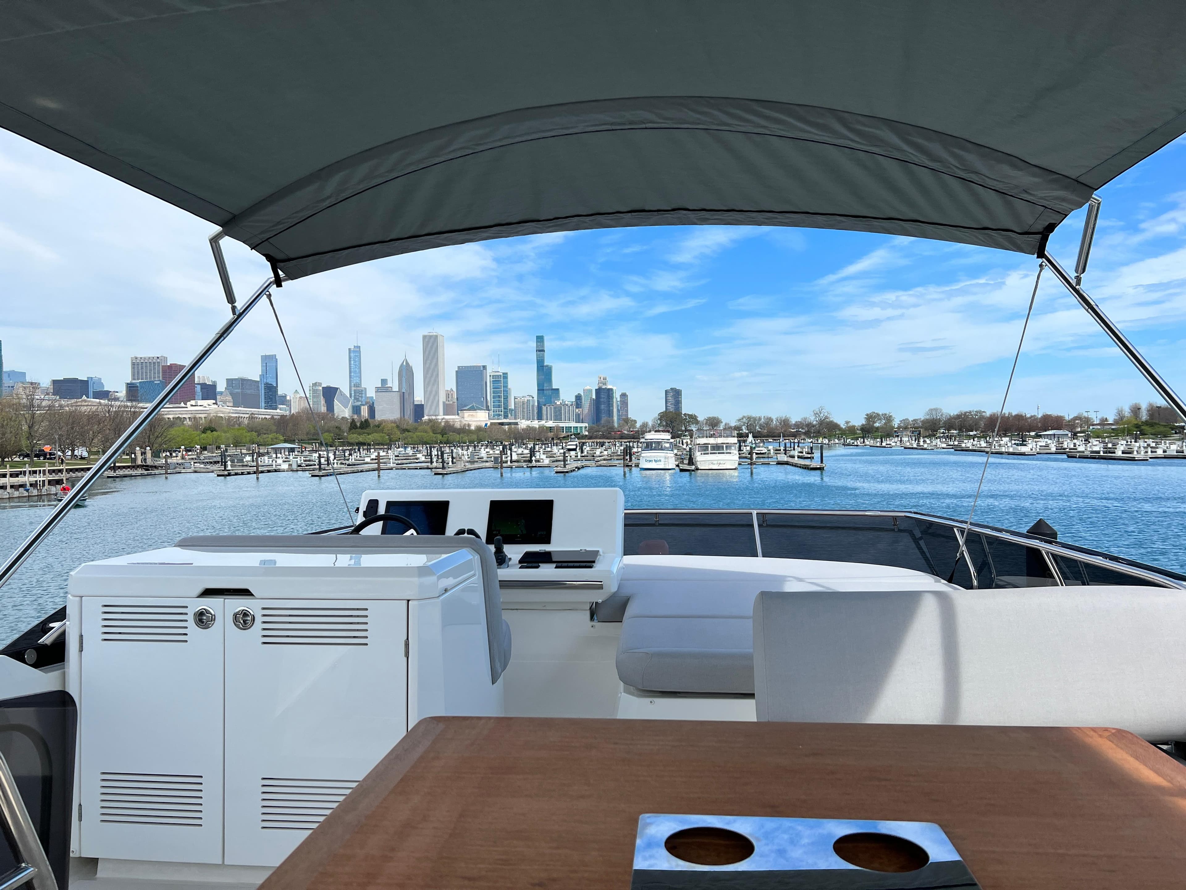 Prestige 520 Flybridge 2024 yacht with city skyline view, under a canopy on calm waters.