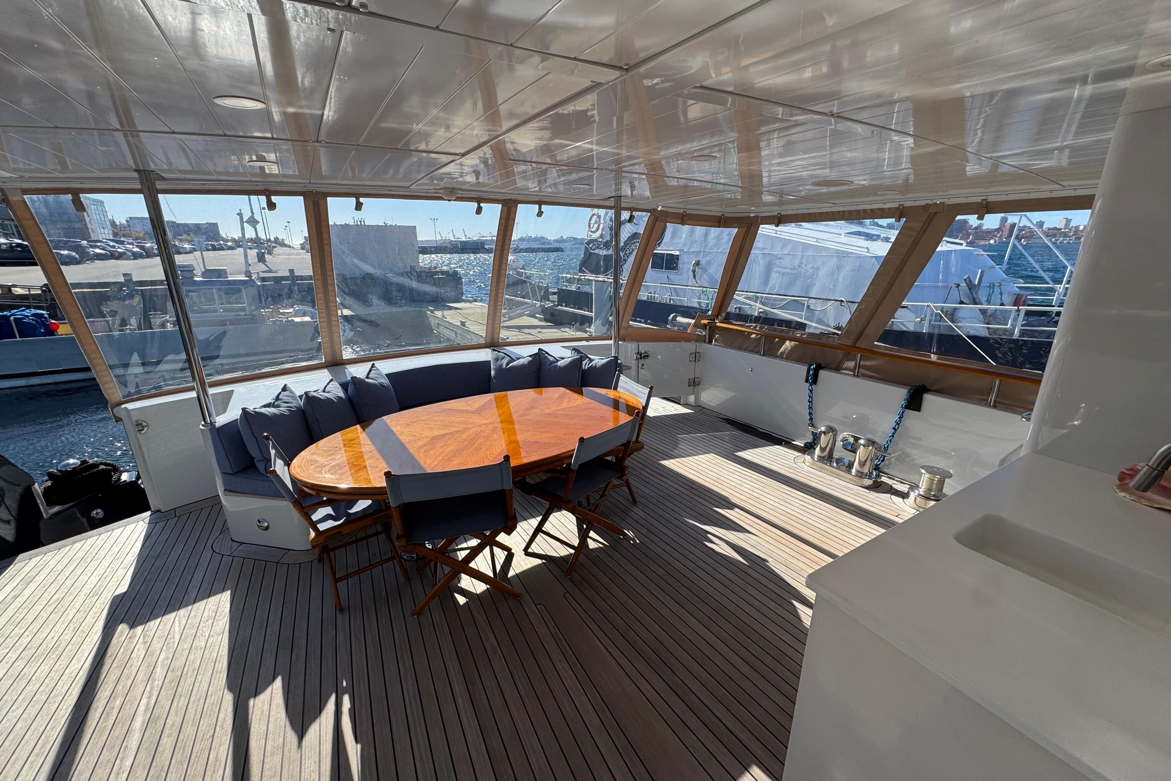 Luxurious yacht deck with wooden table, cushioned seating, and panoramic harbor views. Doogersbank Vipack 2001.