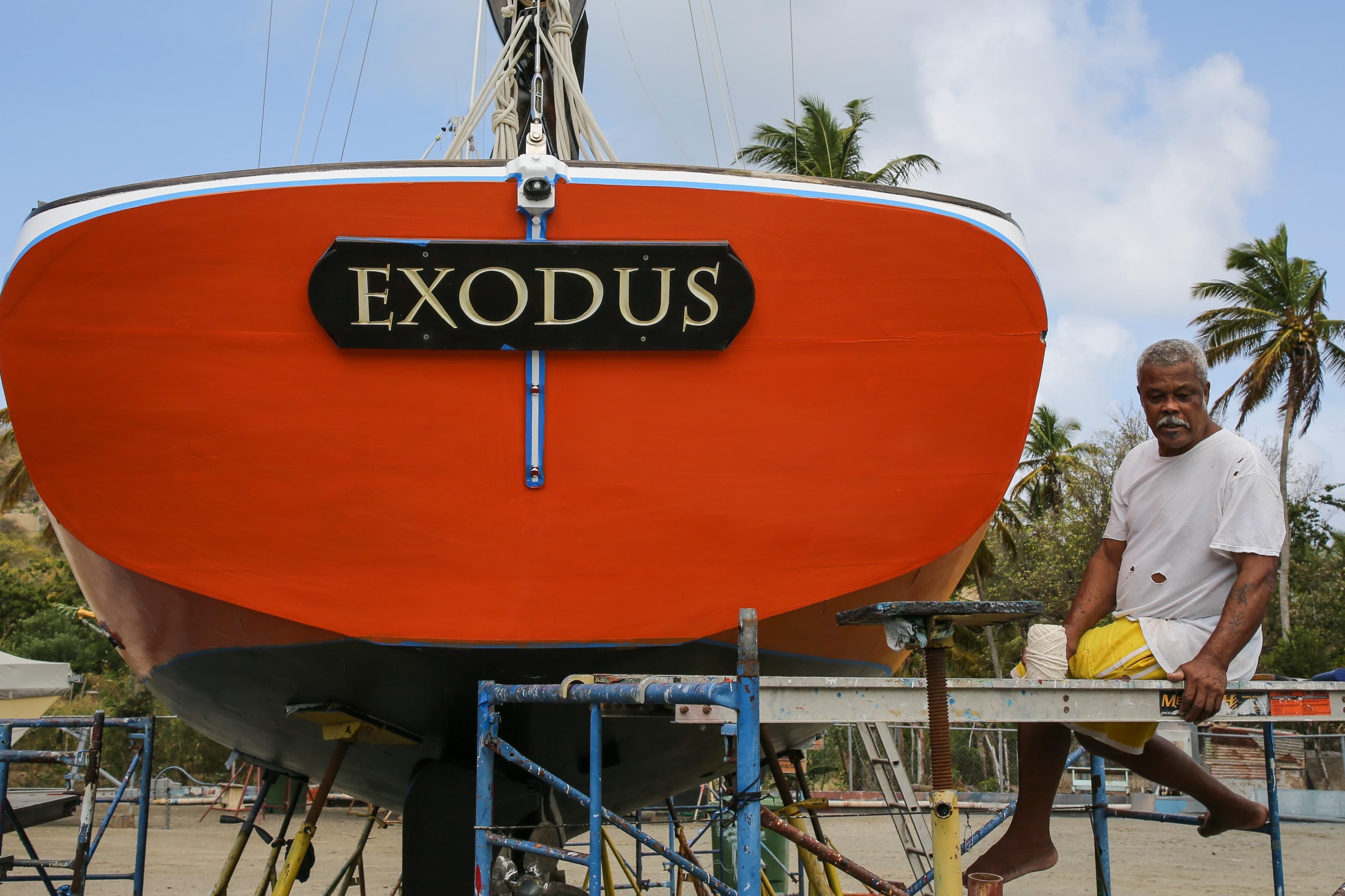 Man sitting beside the vibrant orange 2013 Custom Carriacou Sloop 42 named "Exodus."