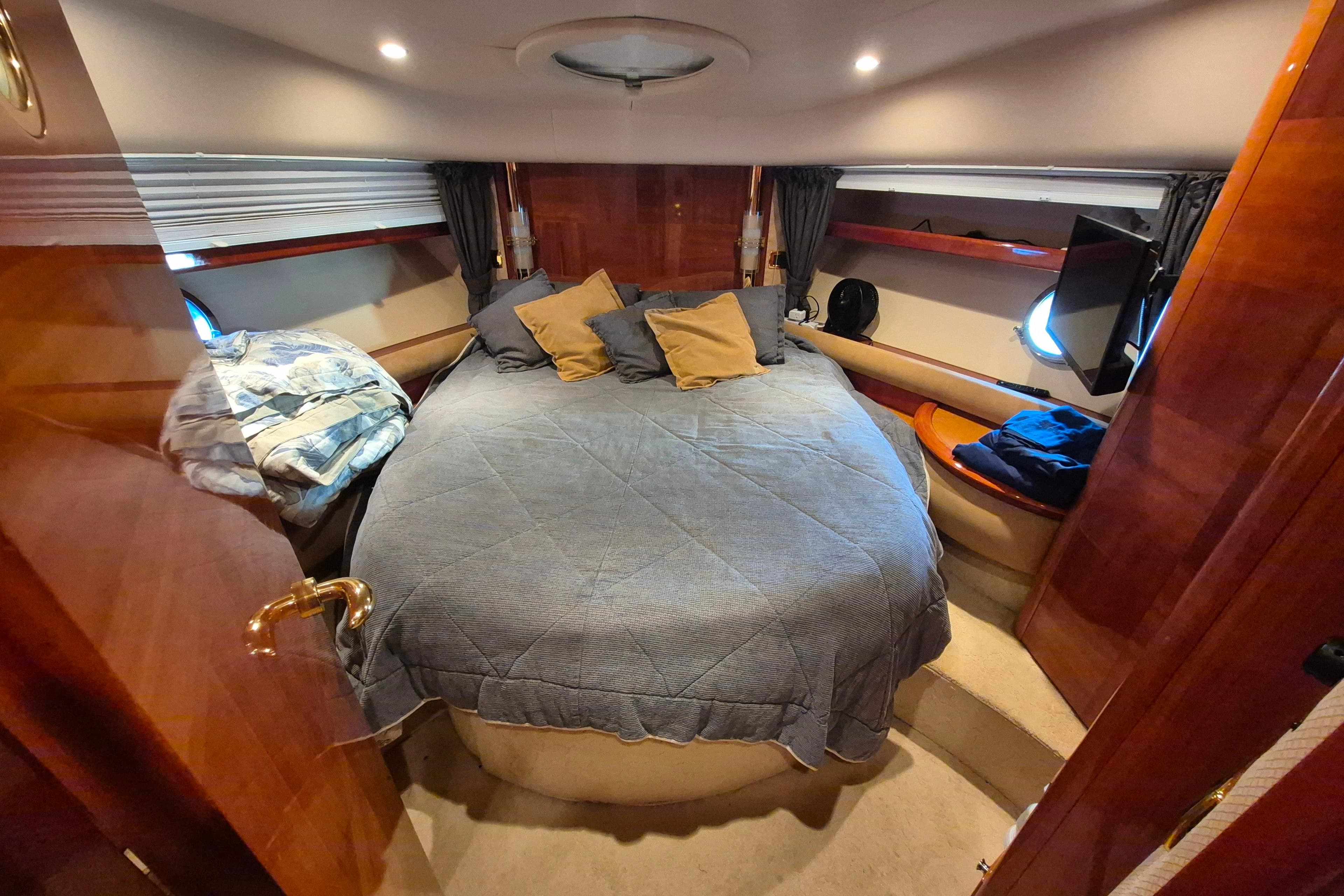 Luxurious bedroom interior of a 2004 Azimut 55E yacht with cozy bedding and elegant wood finishes.