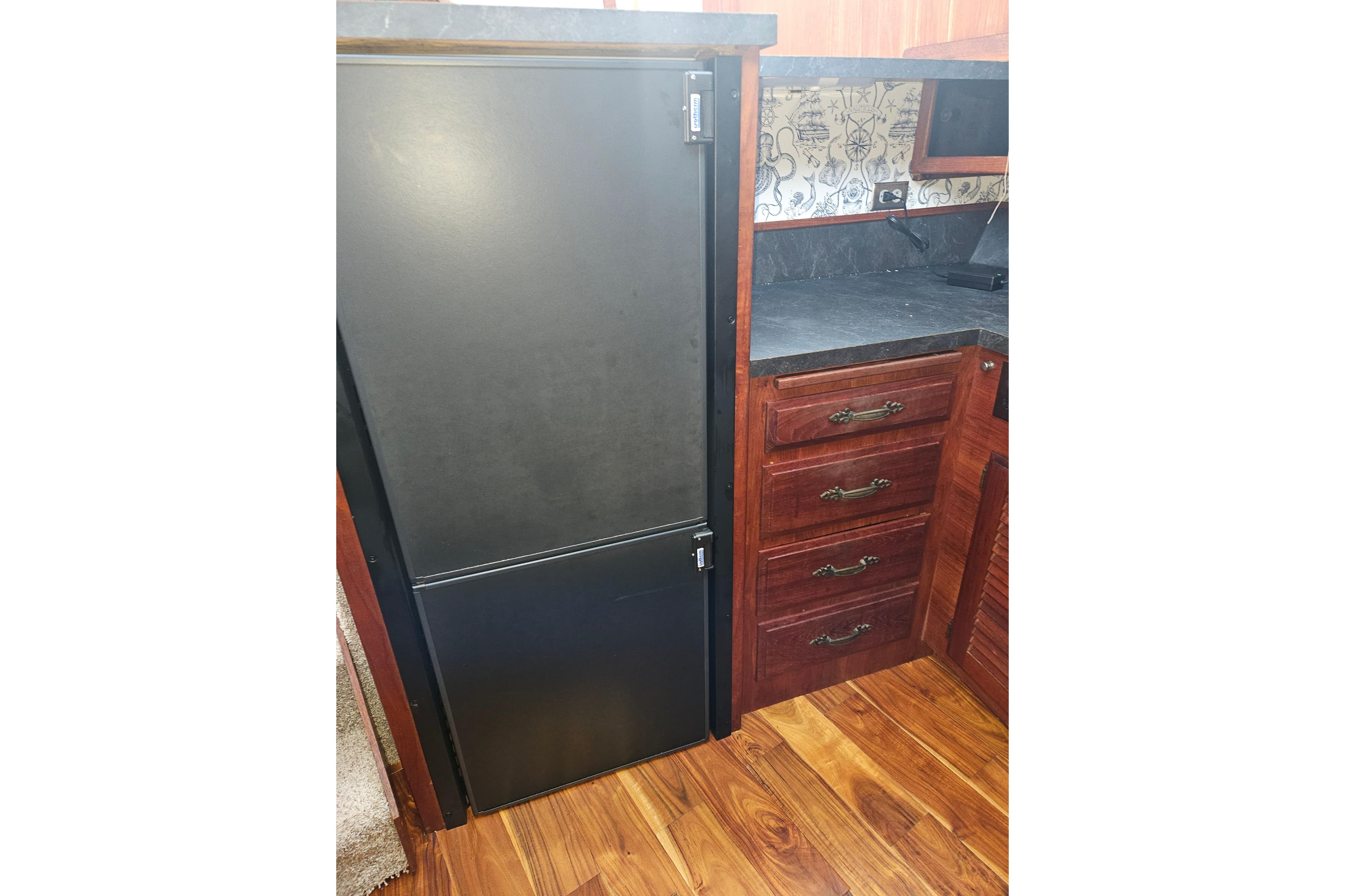 1981 Tollycraft 43 Motor Yacht kitchen with black fridge, wooden cabinets, and patterned backsplash.