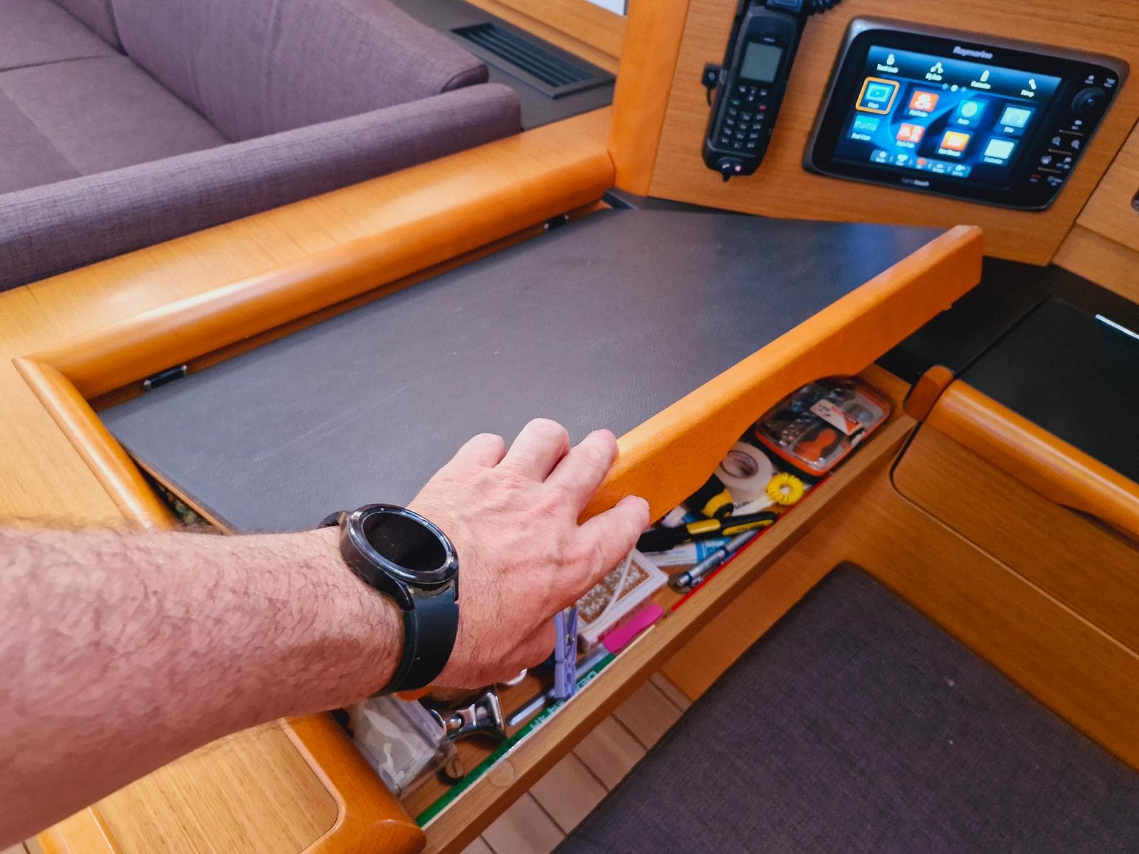 Hand opening a drawer on a 2015 Jeanneau 53 yacht, revealing navigation tools.