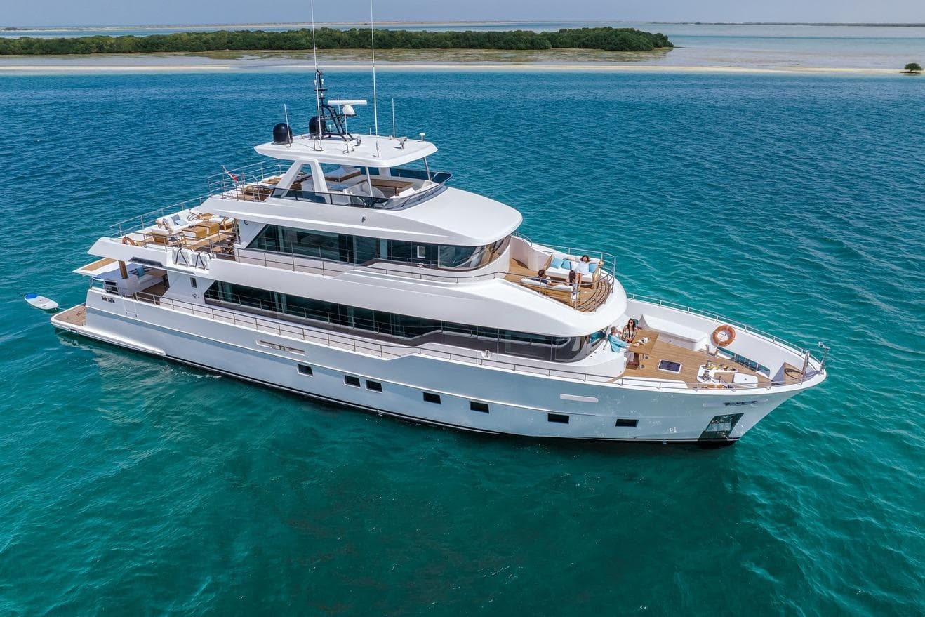 Luxurious 2026 Nomad 101 yacht cruising in clear blue waters near a sandy shoreline.
