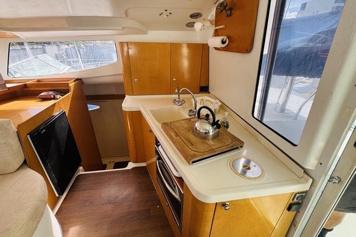 Compact kitchen in a 2010 Fountaine Pagot Mahe catamaran with wooden cabinets and a kettle.