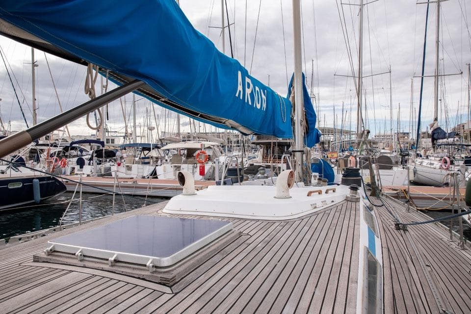 1983 Nautor Swan 65 yacht docked in a marina, featuring a wooden deck and blue sail cover.